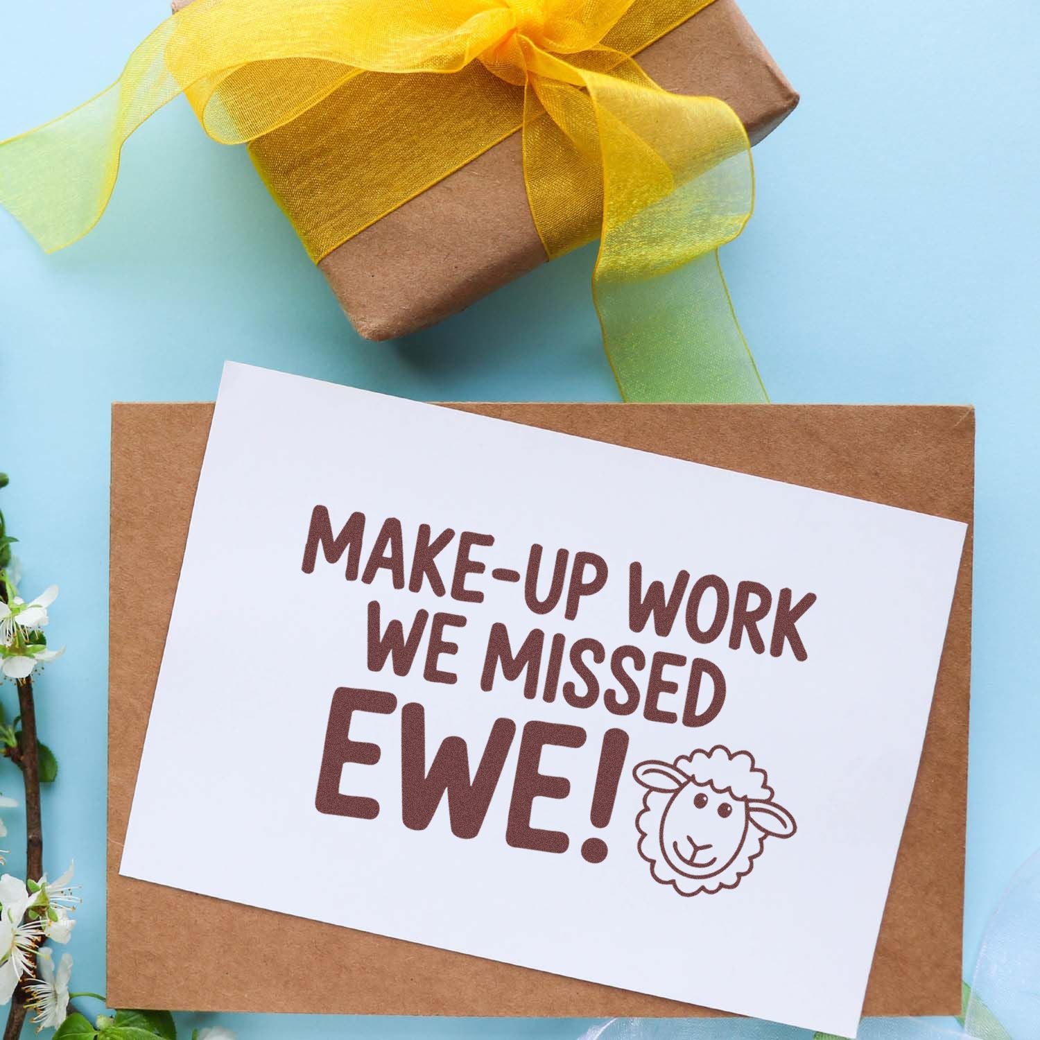 Brown stamp-and-seal card on kraft envelope with MAKE-UP WORK WE MISSED EWE! sheep icon, tied with yellow ribbon on blue.