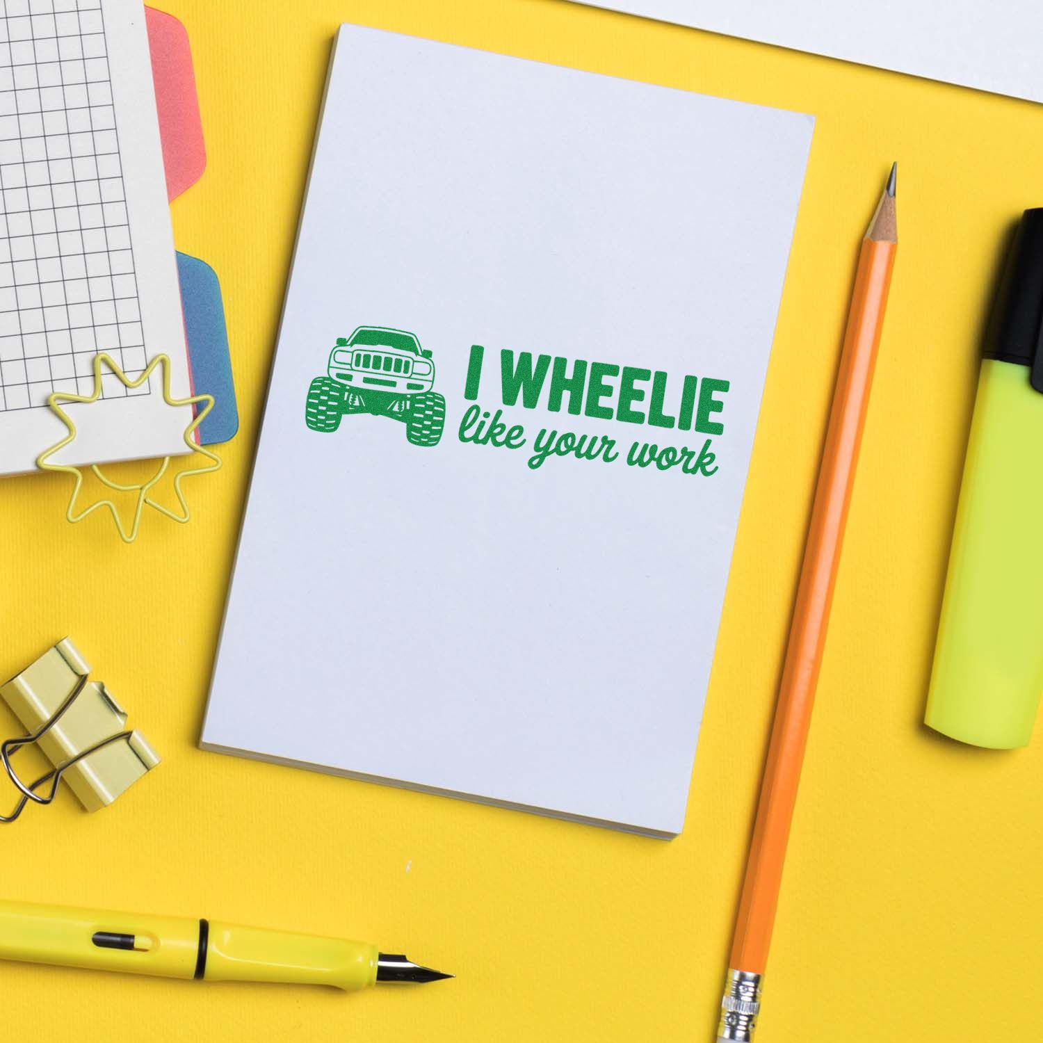Green monster truck stamp and seal with I WHEELIE like your work on white card, on a yellow desk with stationery.