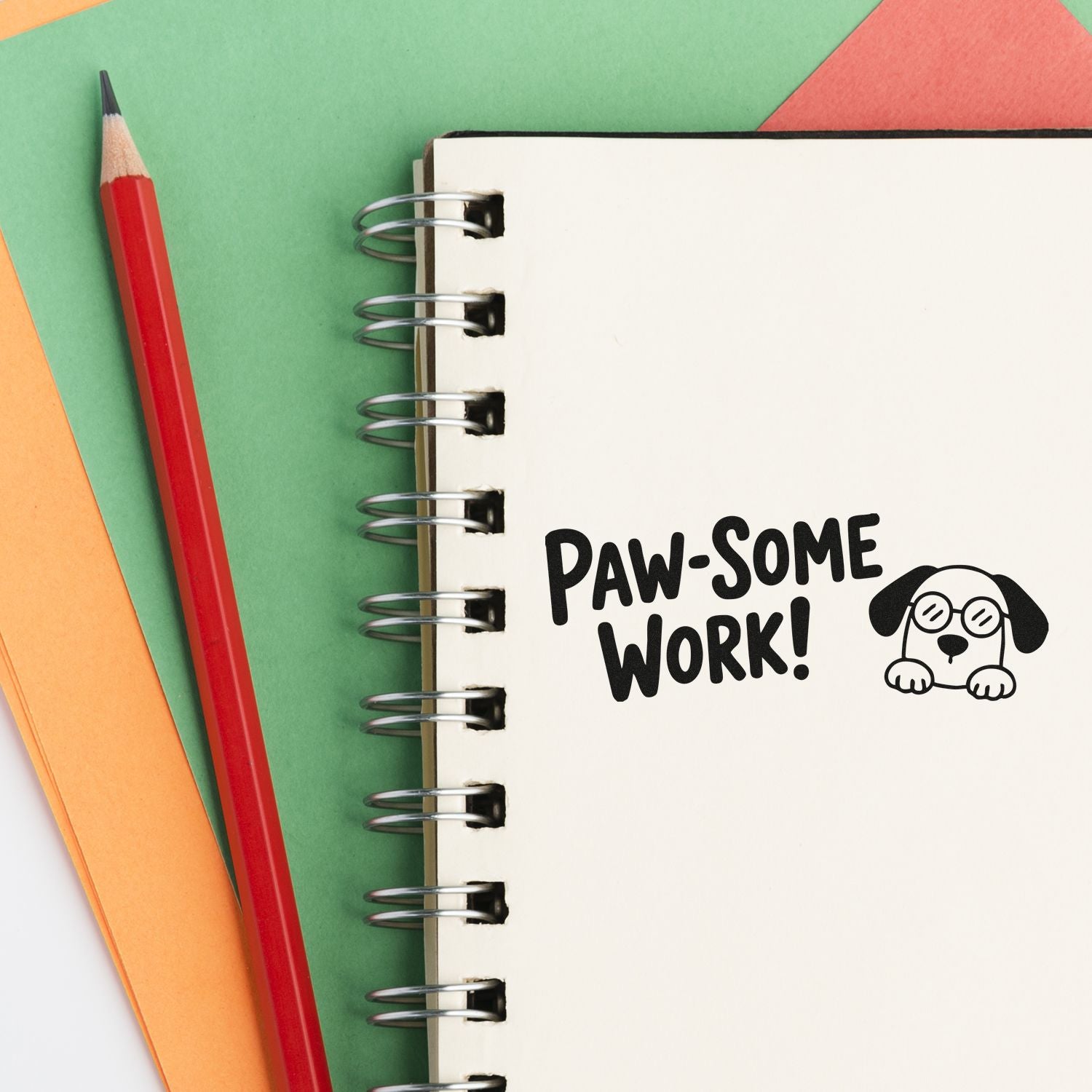 Paw-some Work! dog stamp/seal on spiral notebook, with red pencil and green, orange, pink paper background.
