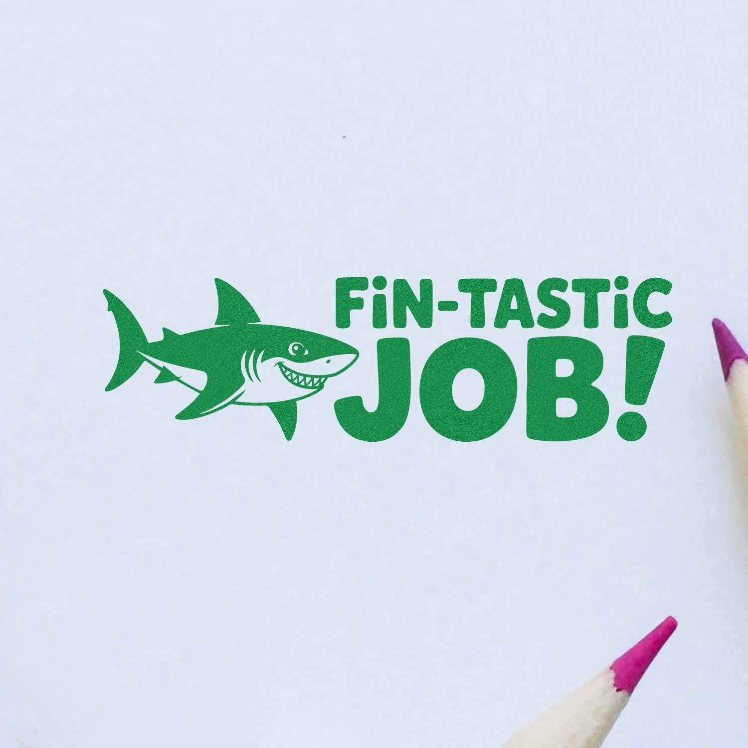 Green shark stamp seal reading FIN-TASTIC JOB! in bright green on white paper, with pink pencil tips at the edges