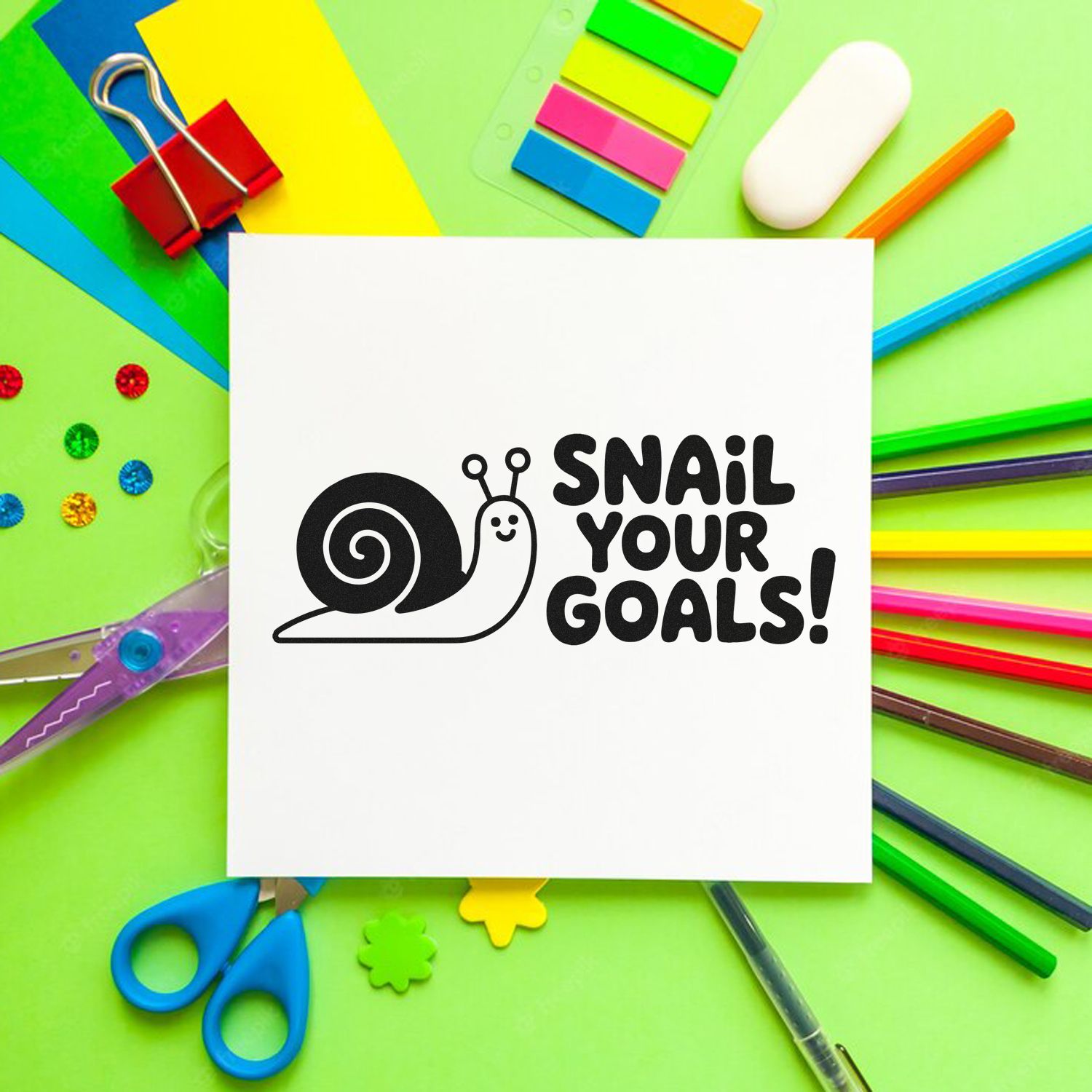 Black snail stamp and seal design reading Snail your goals! on white card, with colorful stationery on a green background.