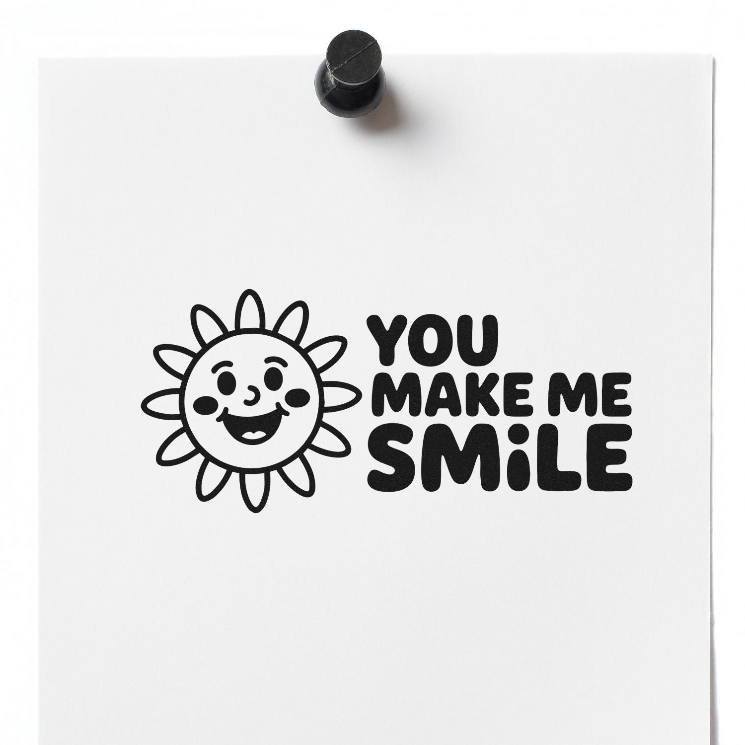 Black rubber stamp and seal on white paper with smiling sun and bold You Make Me Smile text.