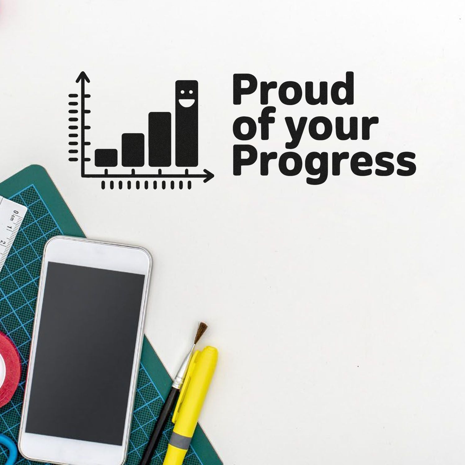 Black self-inking stamp and seal reading Proud of your Progress with bar chart icon on white, beside craft tools.