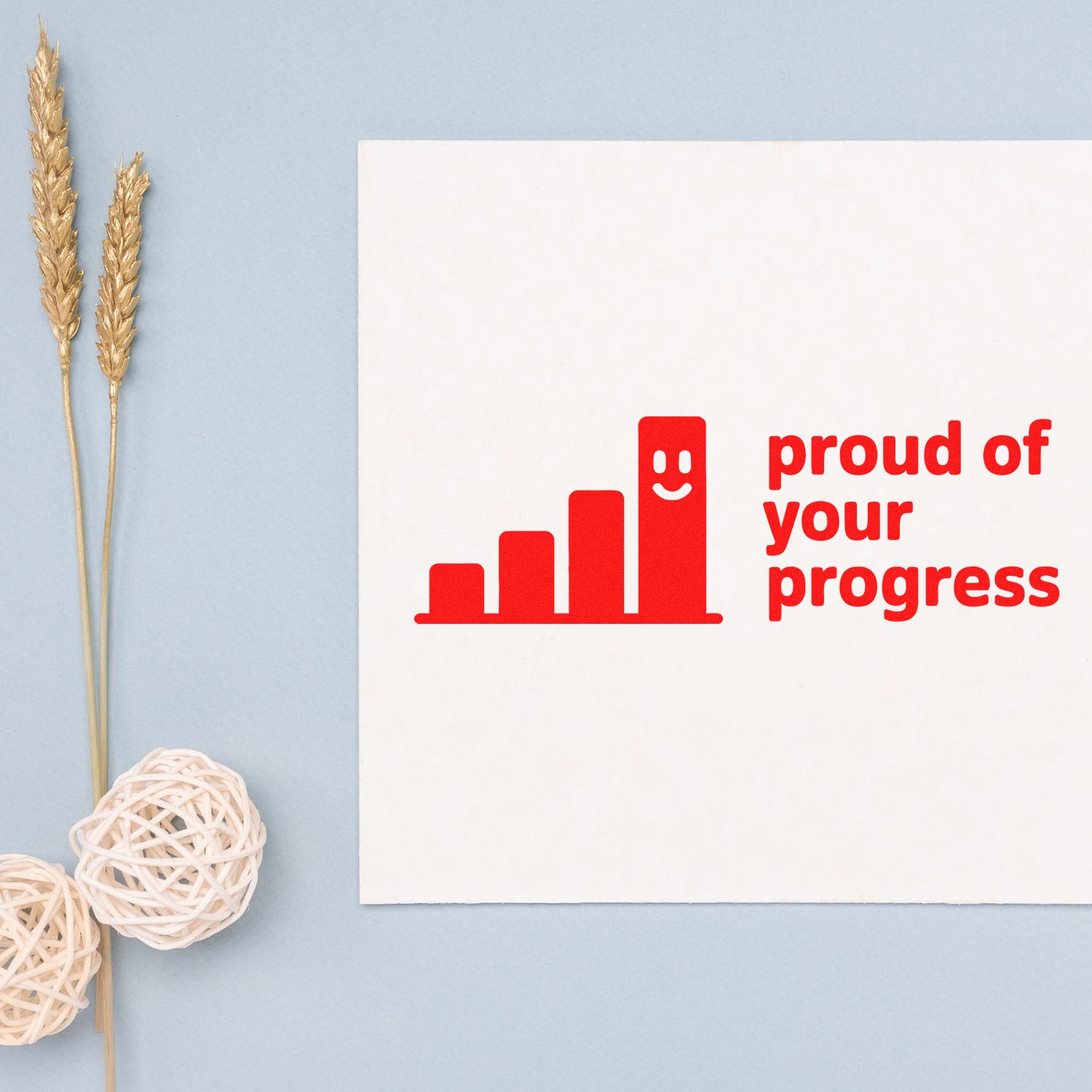 White card with red stamp and seal reading proud of your progress, beside gold wheat stems on a pale blue background.