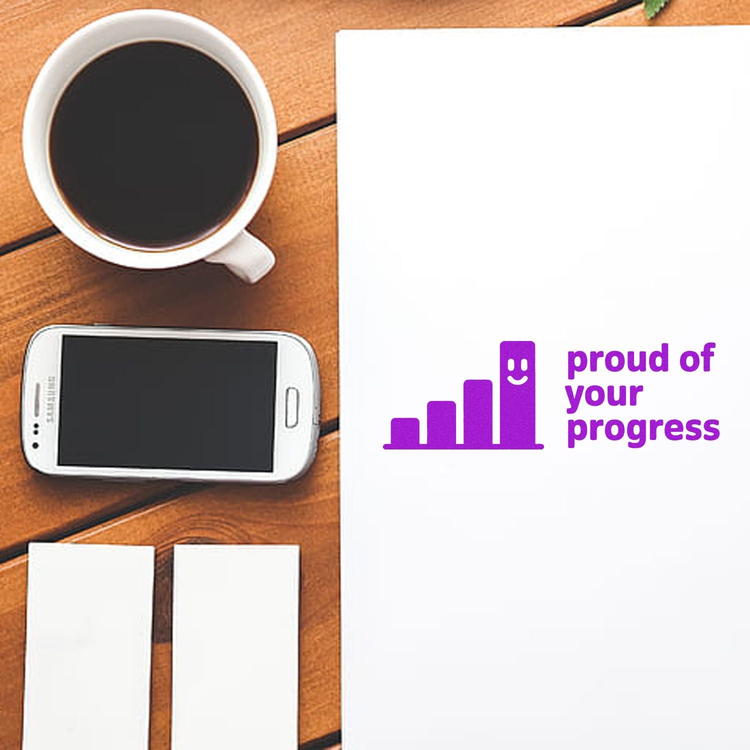 Purple "proud of your progress" stamp and seal on white paper, beside blank cards, coffee, and smartphone on a wooden desk.