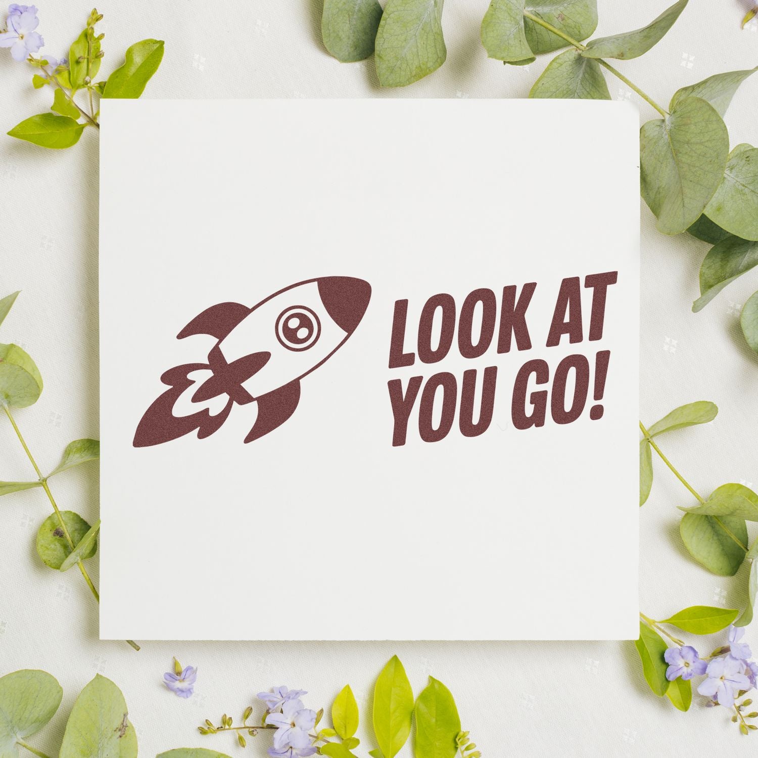 Maroon rocket stamp and seal with LOOK AT YOU GO! on white card, framed by green leaves and purple flowers.