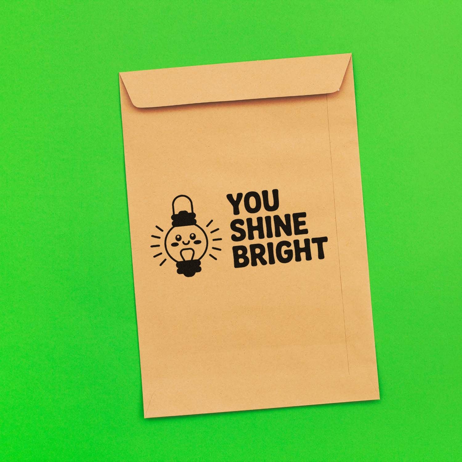 Tan kraft envelope with black You Shine Bright stamp seal and smiling light bulb on bright green background.
