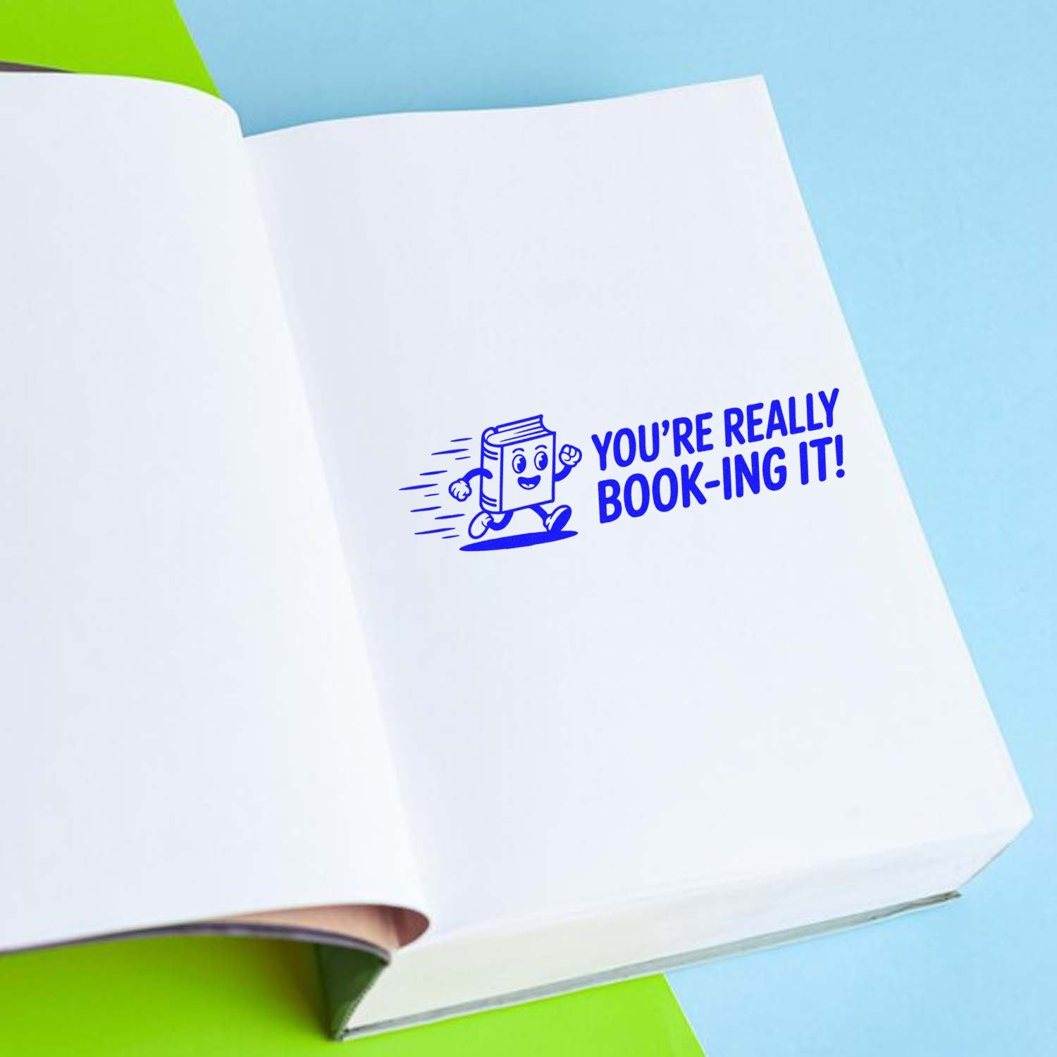 Blue book-shaped stamp and seal reading Youre really book-ing it! on open white pages with light blue and green accents.