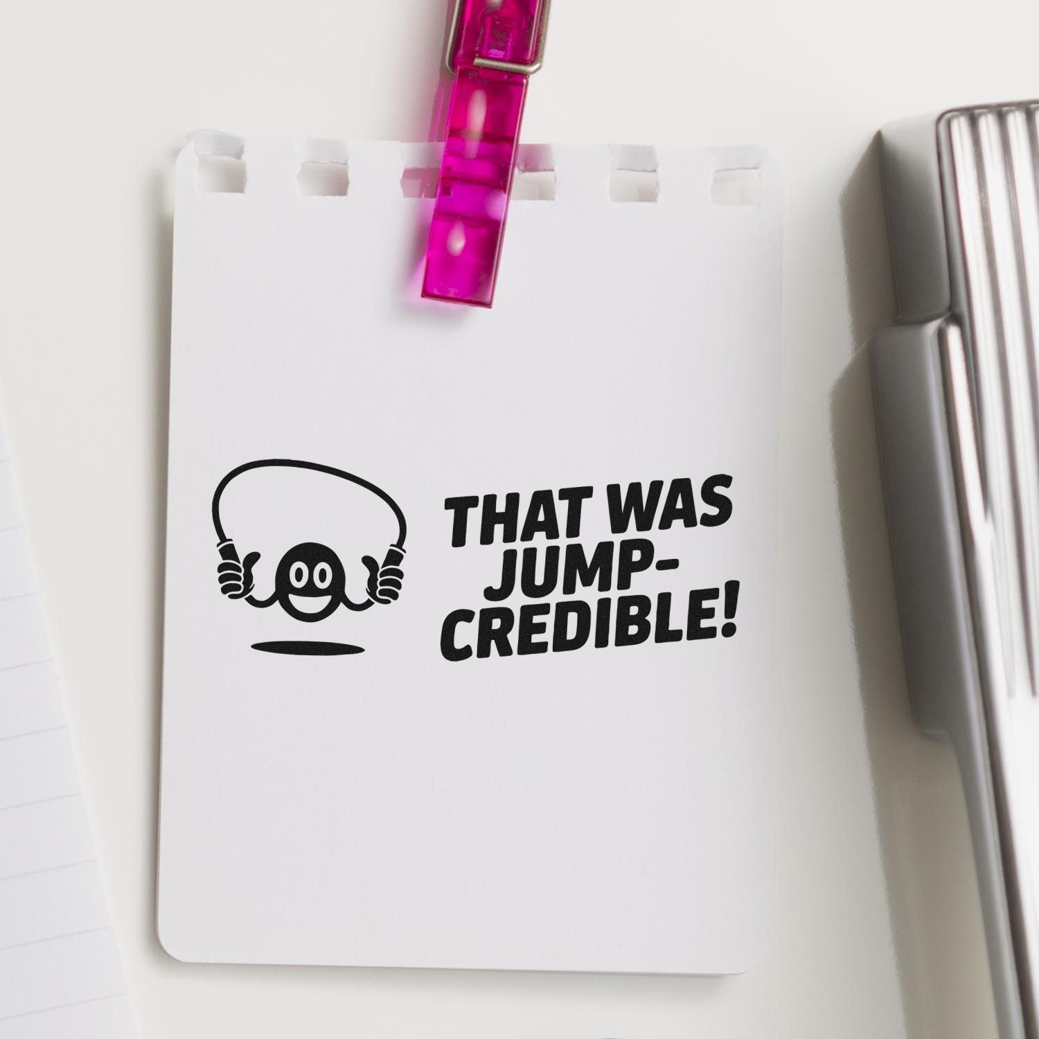 White stamp and seal product sheet with black THAT WAS JUMP-CREDIBLE! graphic, pink clip, and silver stamp tool.