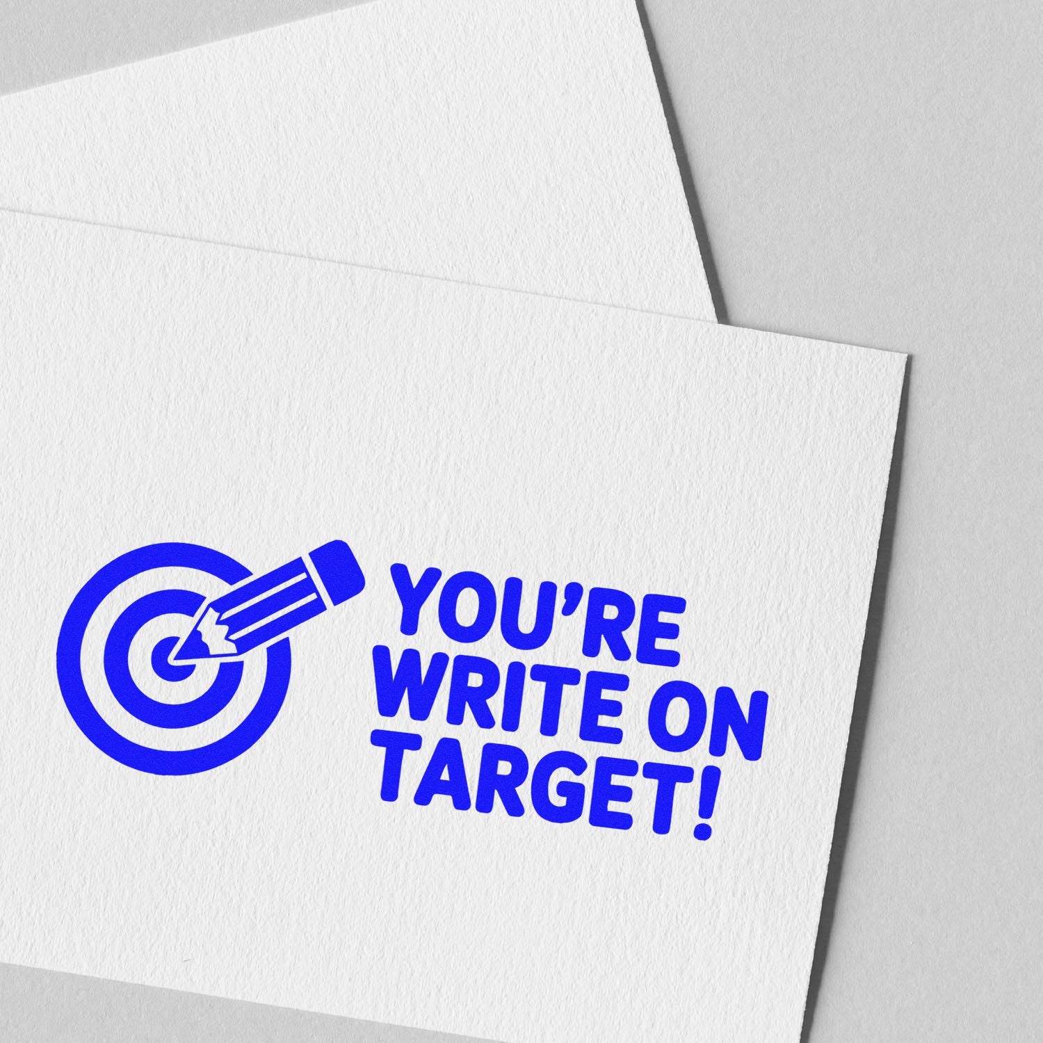 Blue stamp-style seal with target and pencil on white textured paper reading Youre write on target!