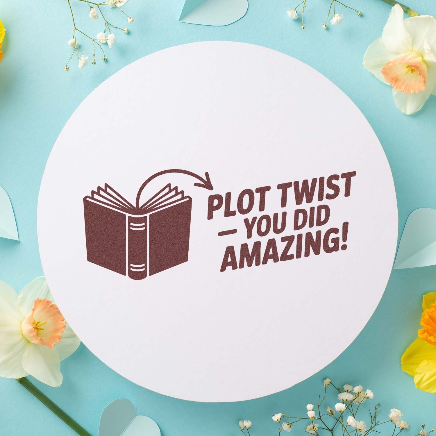 Brown book stamp on a white round seal with Plot TwistYou Did Amazing! pastel blue floral background.