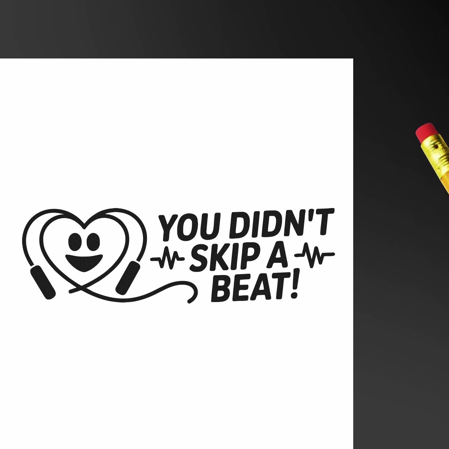 Black heart-stethoscope rubber stamp reading You Didnt Skip a Beat! on white, beside a yellow pencil.