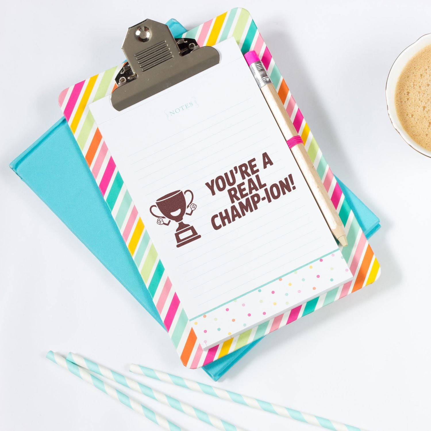 Clipboard notepad with brown trophy stamp seal, pastel striped border, turquoise binder, pencil, and coffee cup.