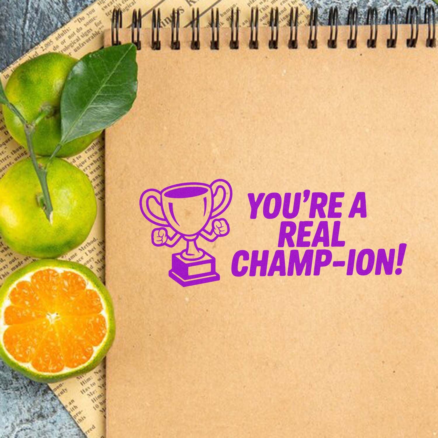 Purple custom stamp with trophy and Youre a Real Champ-ion! on tan notebook page, accented by green and orange citrus.