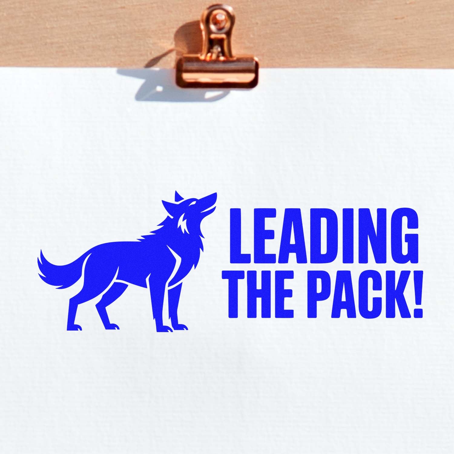 Blue wolf stamp and seal reading LEADING THE PACK! on white paper, clipped to a copper clipboard.
