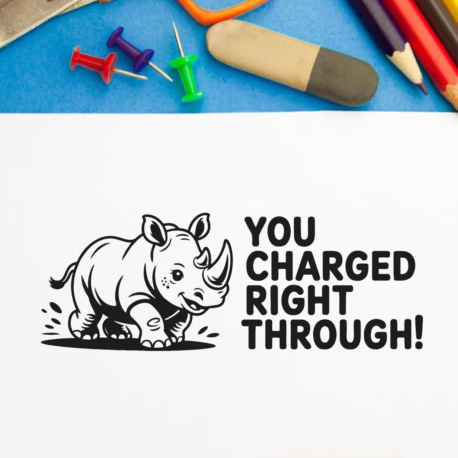 Black rhino stamp seal with You Charged Right Through text on white, on a blue background with colorful push pins and pencils.