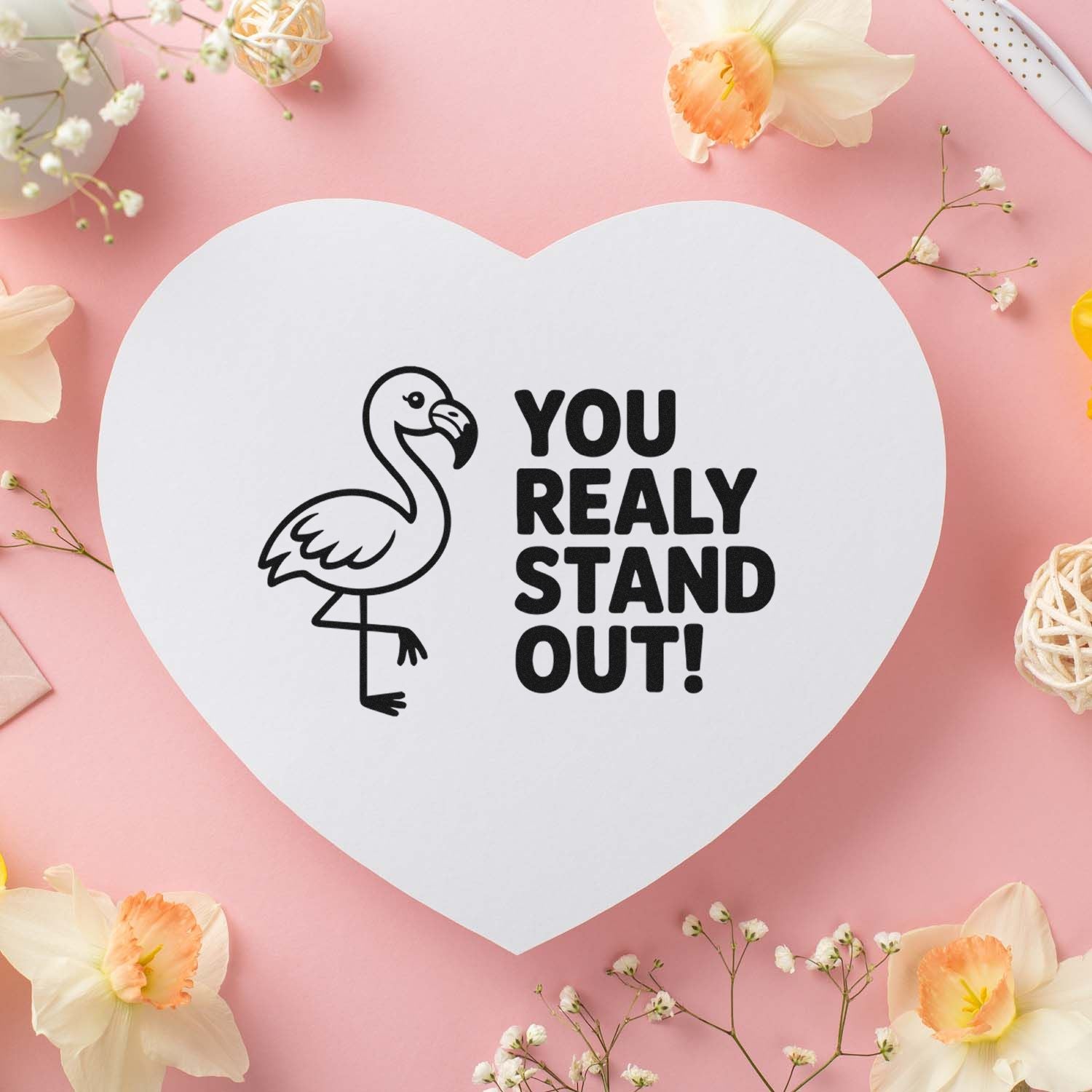Heart-shaped white stamp seal with flamingo and You really stand out! on pink background with flowers.