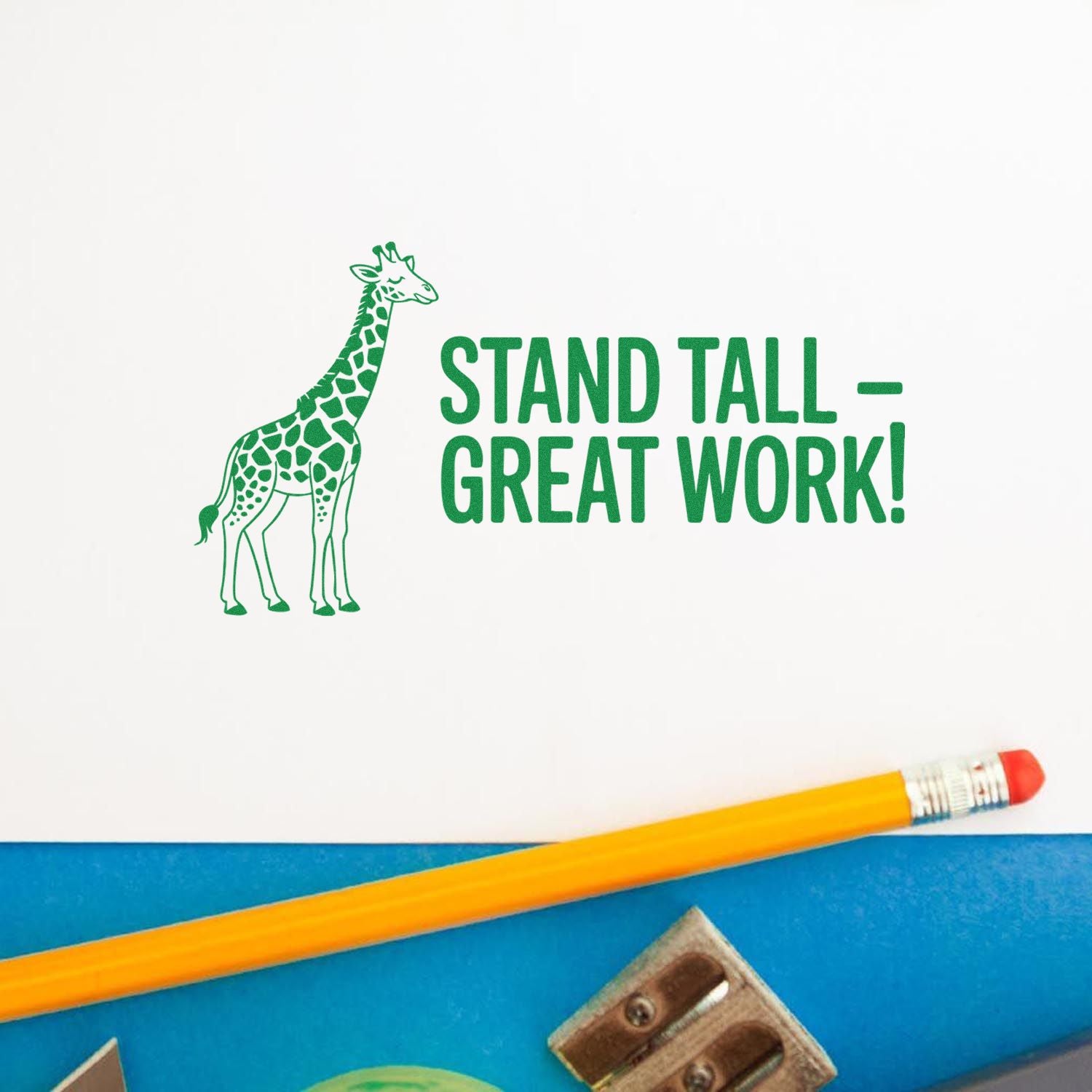 Green giraffe rubber stamp reading Stand Tall  Great Work! on white paper, with yellow pencil on a blue surface.