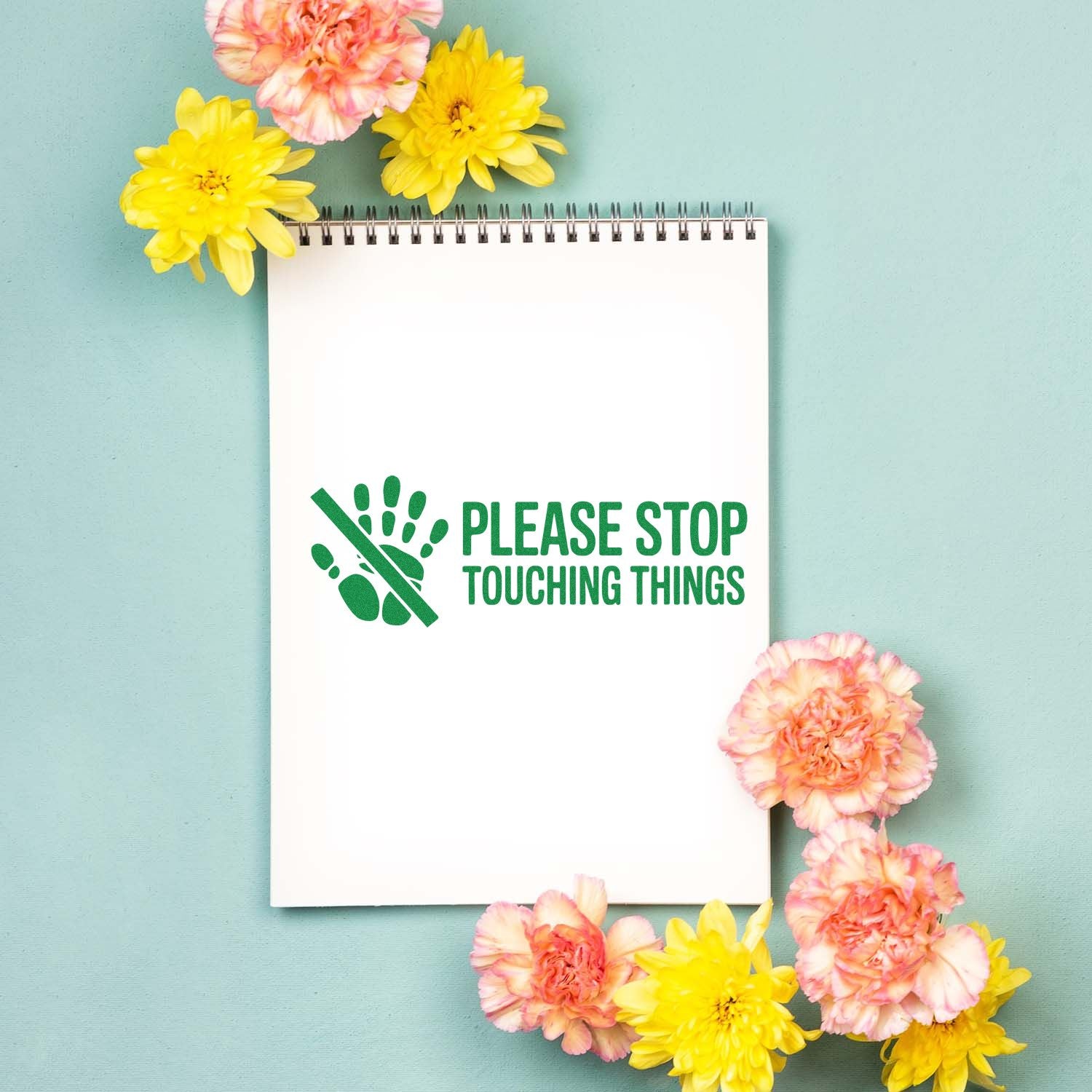 White spiral notebook with green Please Stop Touching Things stamp, hand icon, and yellow and pink flowers on mint background.