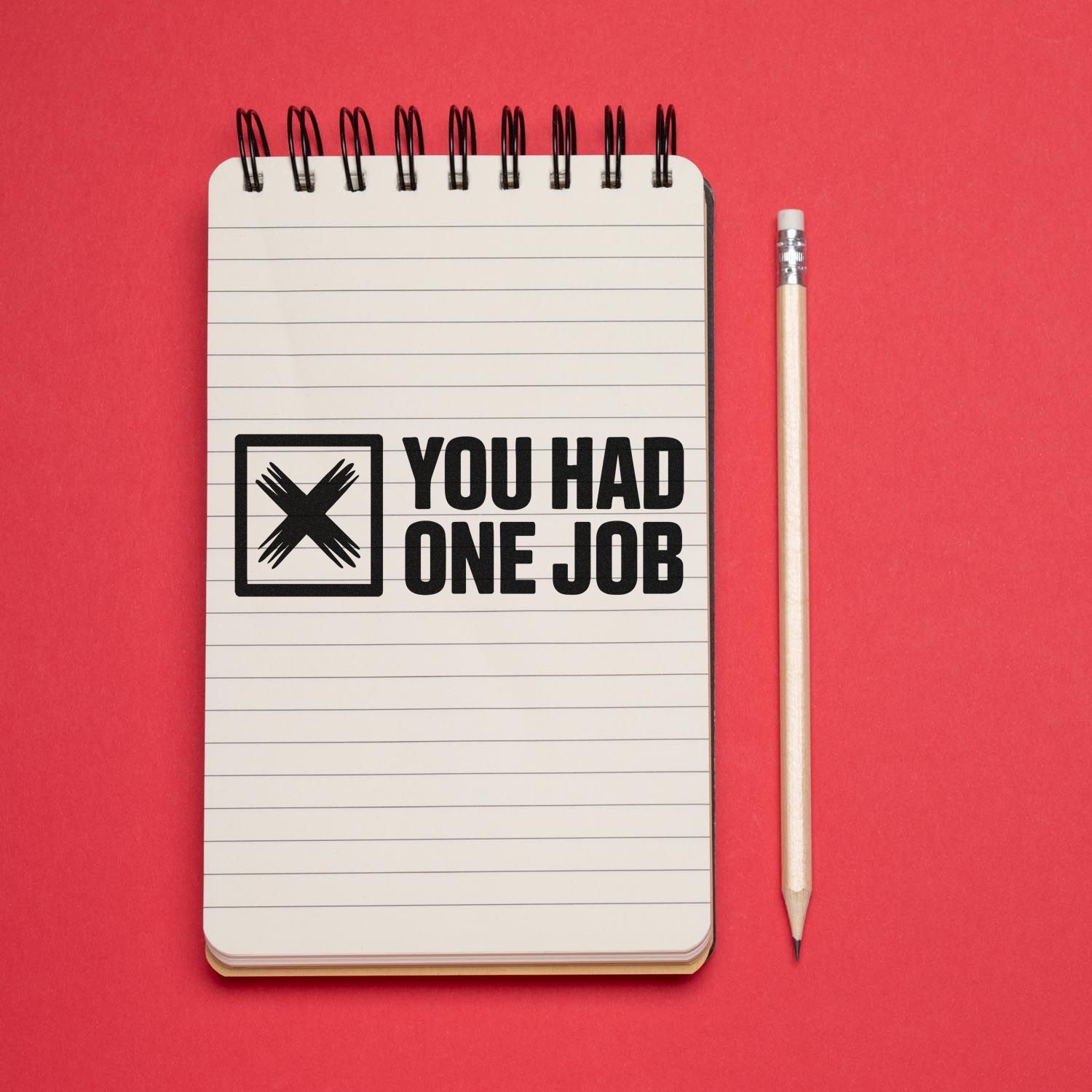 Custom black stamp and seal reading YOU HAD ONE JOB on a lined notebook, with pencil on a red background