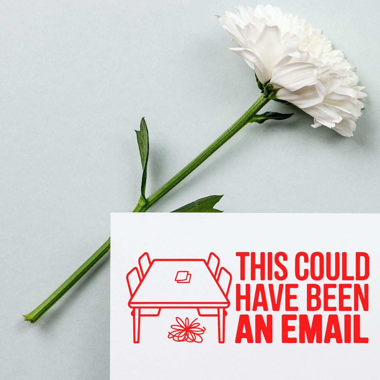 White flower with green stem beside a white card featuring a red custom stamp and seal reading THIS COULD HAVE BEEN AN EMAIL.