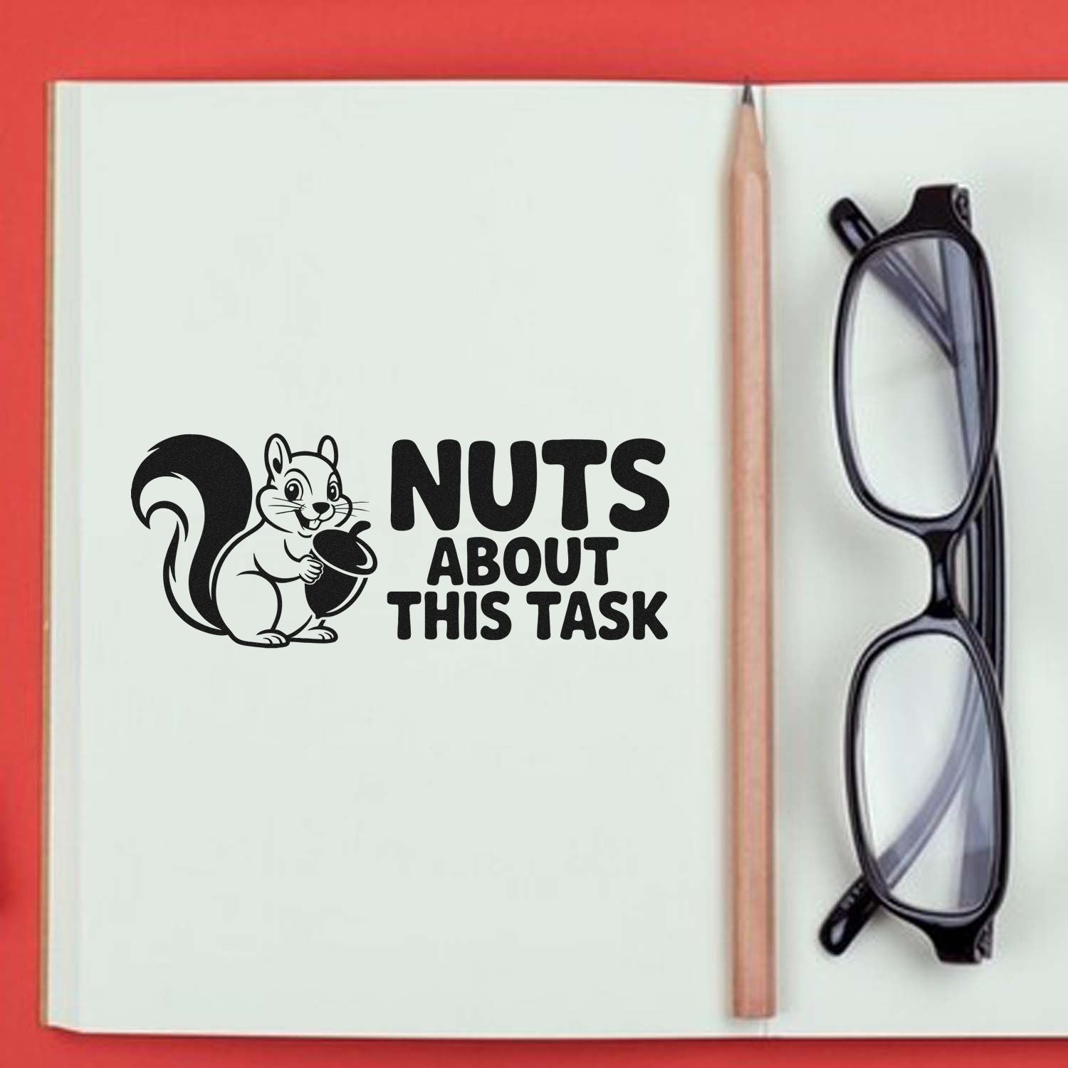 Black custom stamp/seal design with squirrel and acorn, reading Nuts About This Task, on a white notebook beside a pencil and glasses.