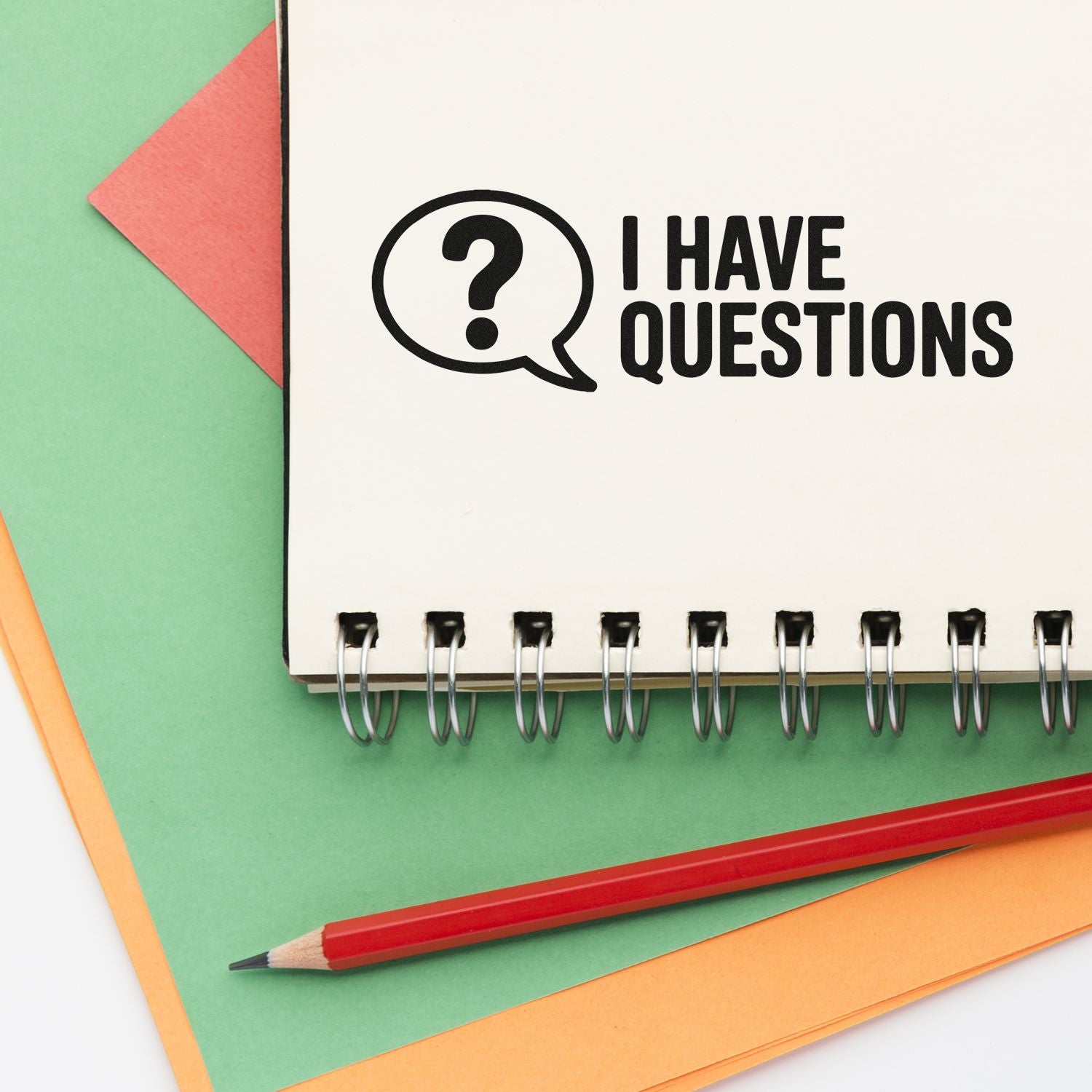 Black I HAVE QUESTIONS stamp and seal design on white spiral notebook with question mark, over green, orange, and red papers.