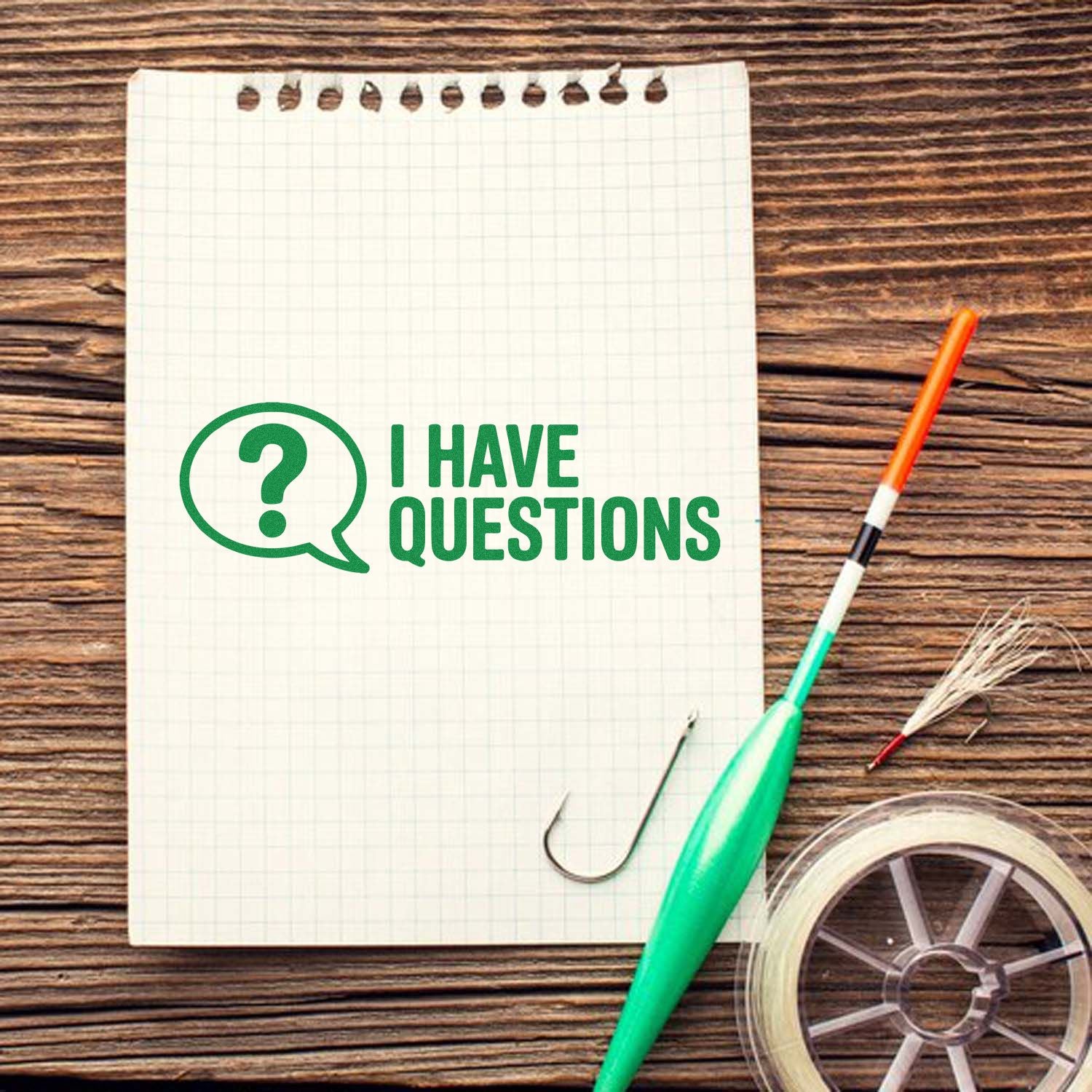Green I HAVE QUESTIONS stamp and seal on graph paper notebook with fishing line spool and hook on wood desk