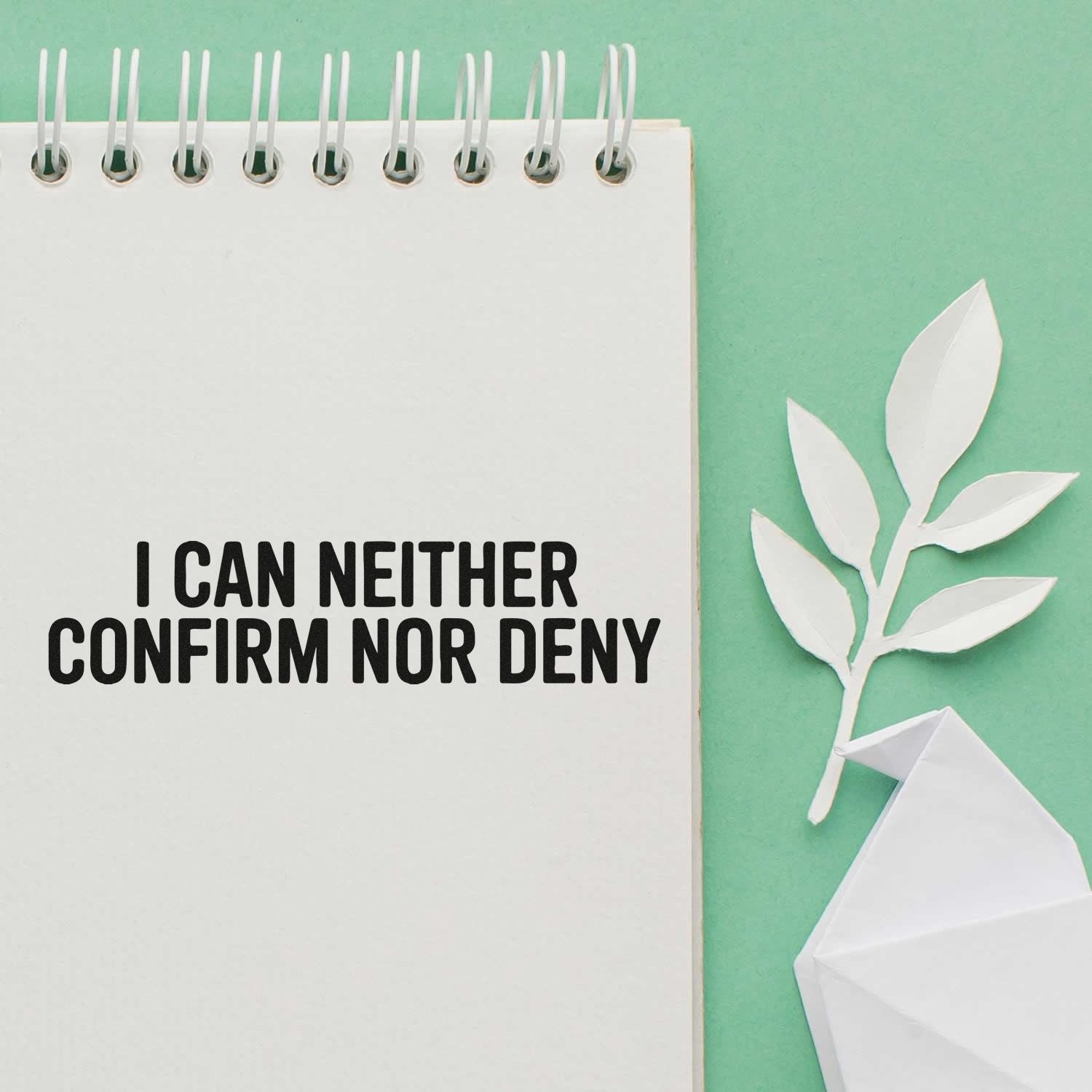 White spiral notebook with bold black stamp-style text, beside a white paper leaf and origami seal on mint green.
