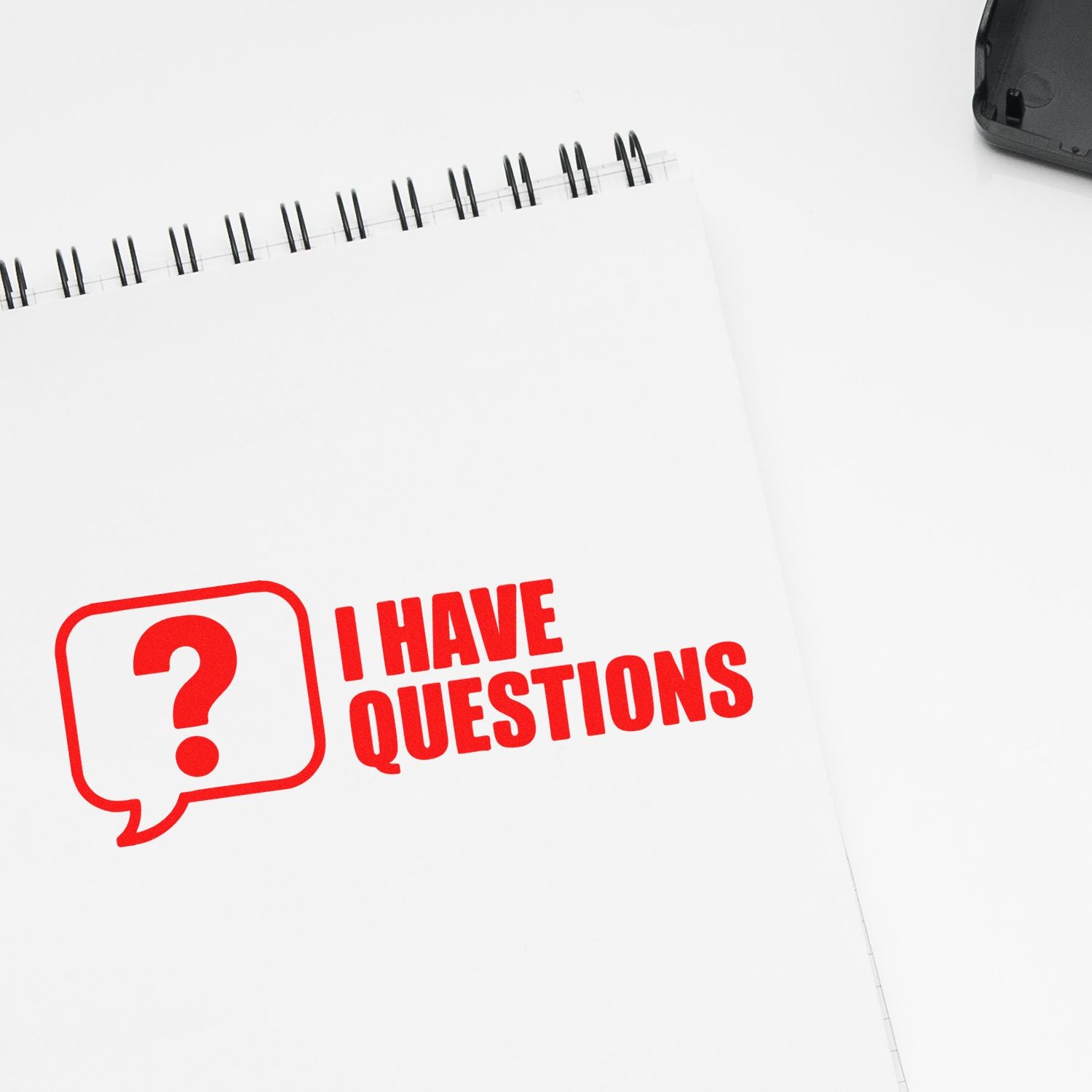 White spiral notebook with bold red I HAVE QUESTIONS stamp and black stamp seal product on a white background.