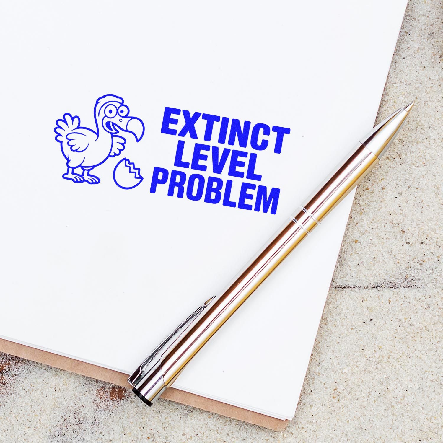 Blue custom stamp and seal reading EXTINCT LEVEL PROBLEM with dodo bird on white paper beside a gold pen.