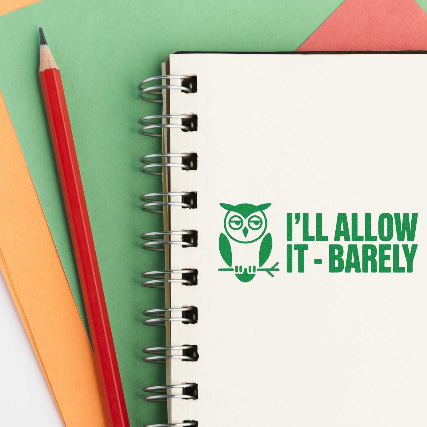 Green owl seal stamp reading Ill allow it - barely on a spiral notebook beside a red pencil