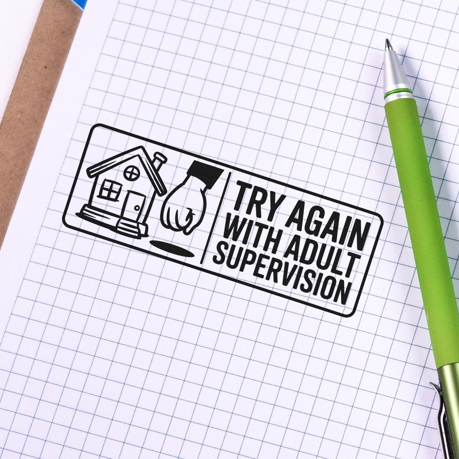 Black rubber stamp seal reading Try Again With Adult Supervision on white grid paper beside a green pen.