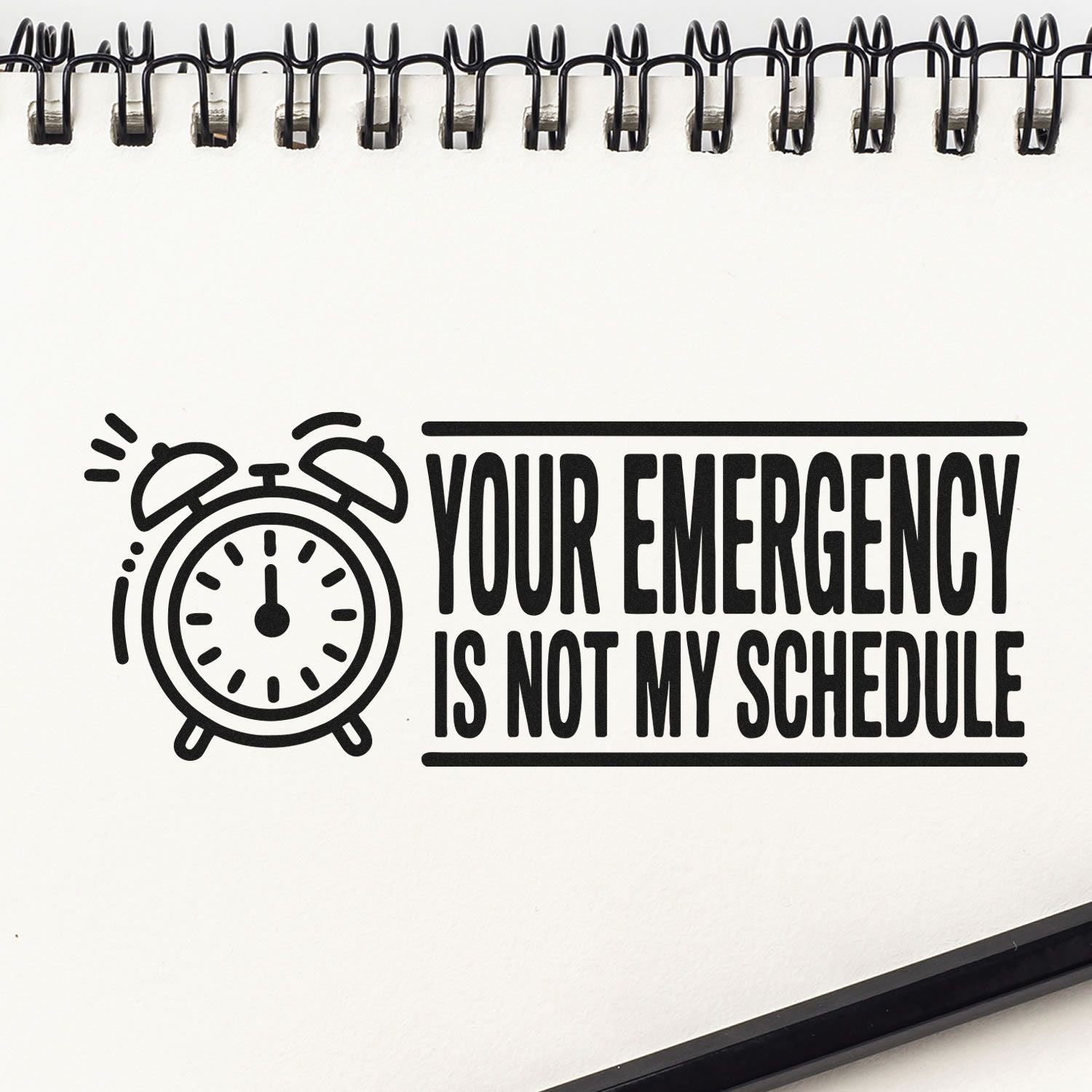 Black stamp seal with alarm clock icon and bold text, Your emergency is not my schedule, on a white notebook page.
