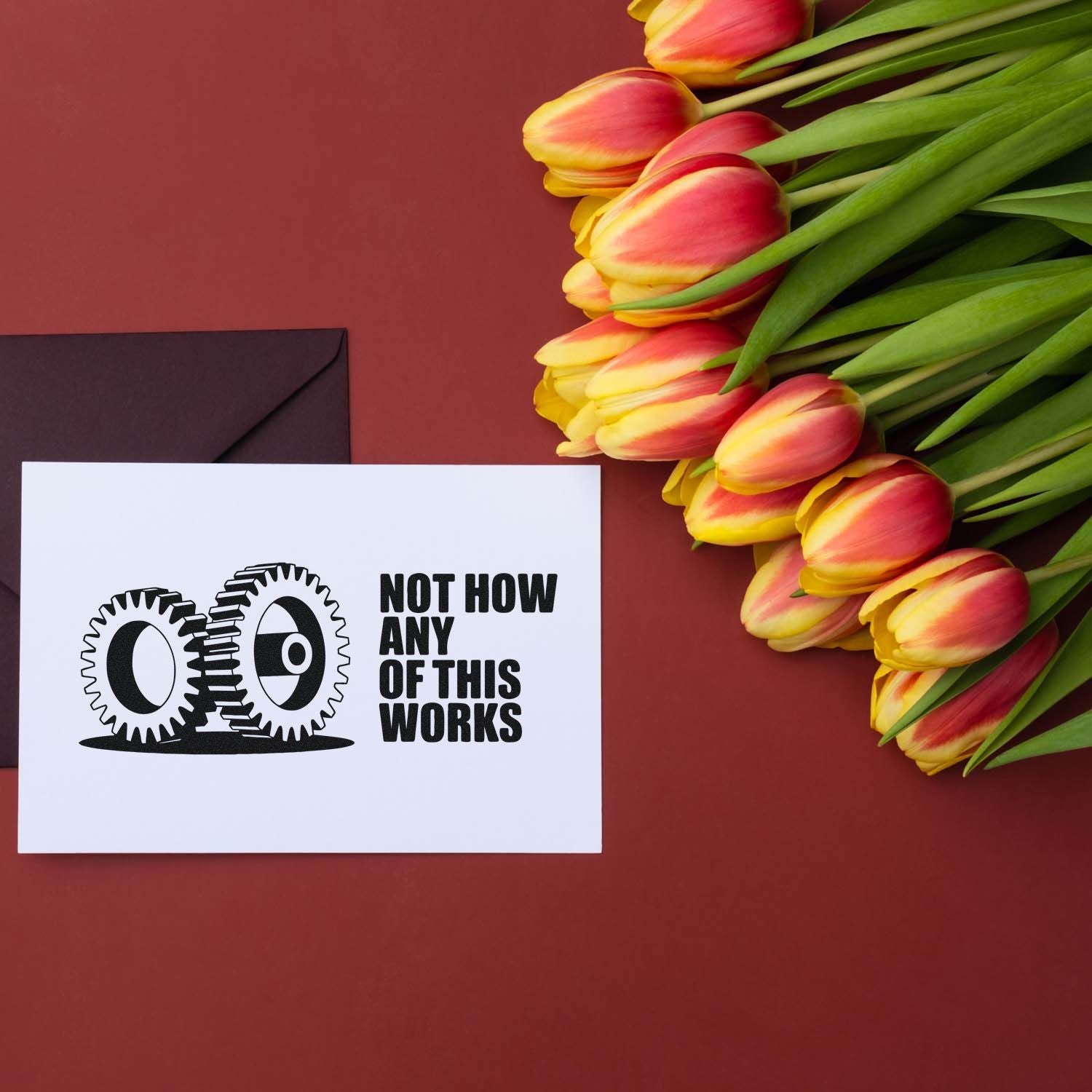 Stamp and seal product card with black gear logo and bold text beside yellow-pink tulips on a burgundy background.