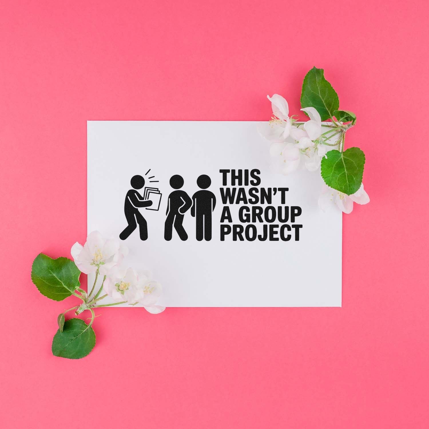 Custom rubber stamp on white card reading This wasnt a group project, with black graphics, white blossoms, and pink background.