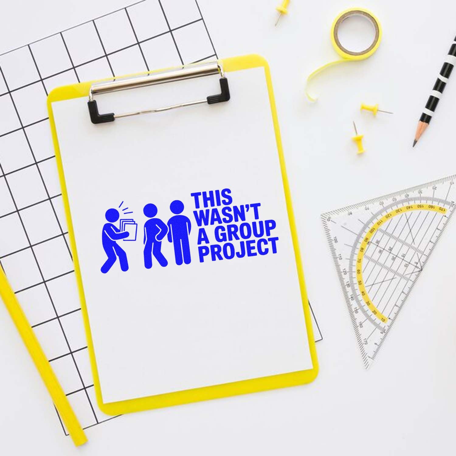 Blue rubber stamp on yellow clipboard reads This wasnt a group project, with drafting tools on a white background.