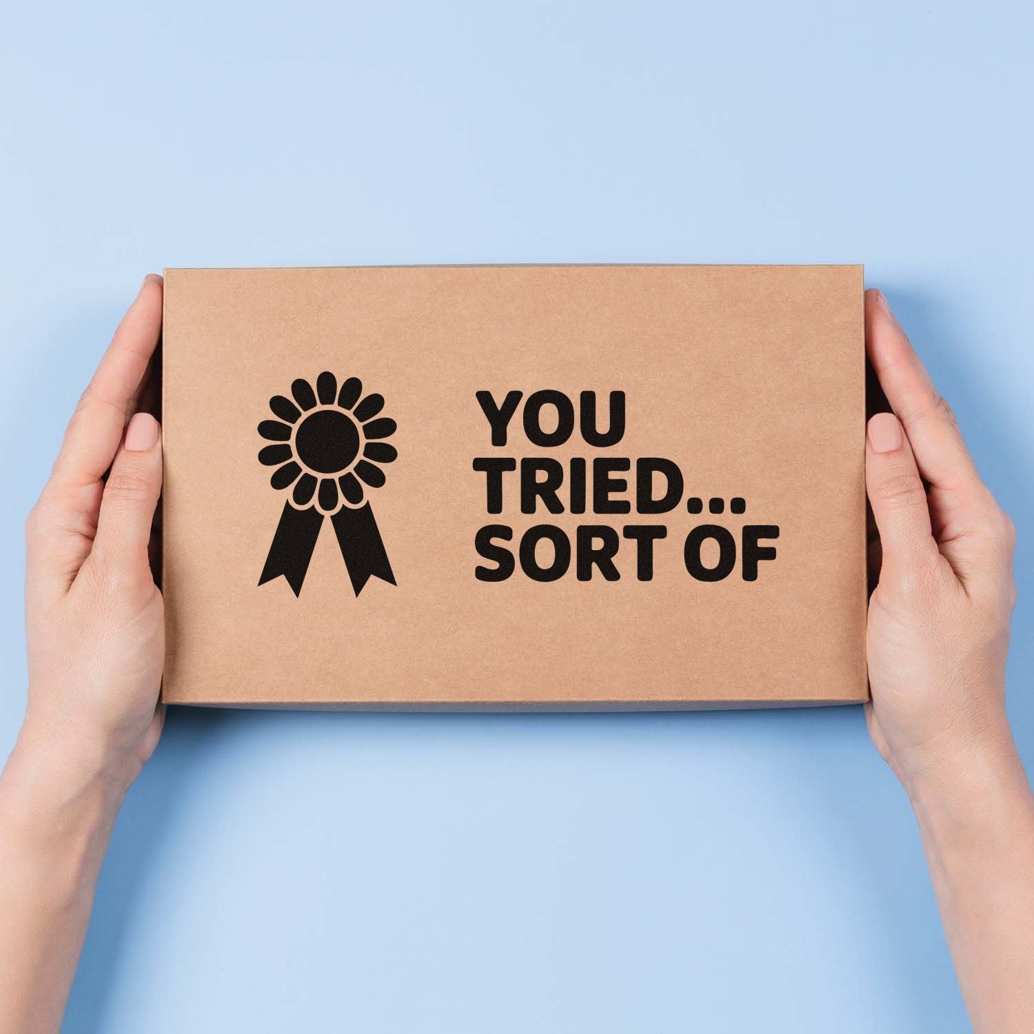 Hands holding kraft box with black award seal stamp reading YOU TRIED... SORT OF on a light blue background.