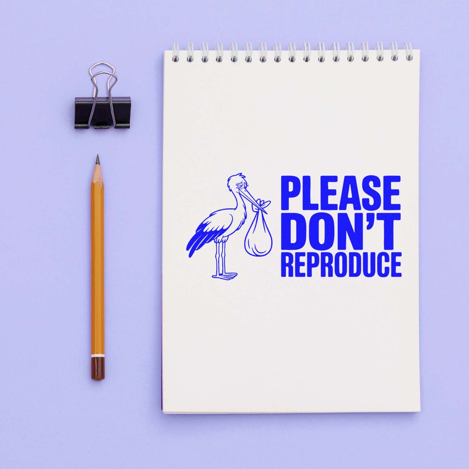 Blue Please Dont Reproduce stamp on white spiral notepad, with stork graphic, beside pencil and binder clip on lavender background.