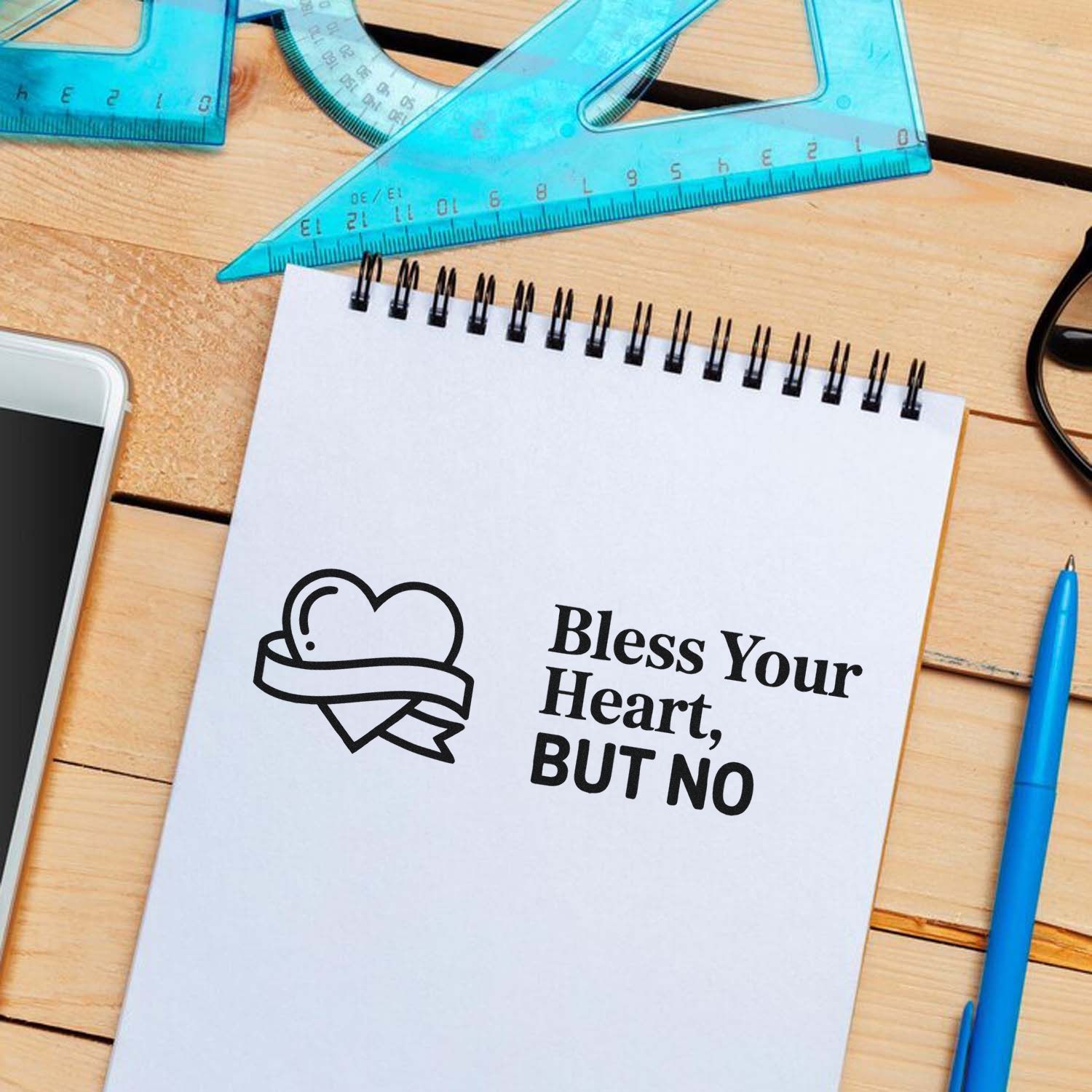 Black stamp seal with heart ribbon and Bless Your Heart, BUT NO on white notepad; blue rulers and pen on wood desk.