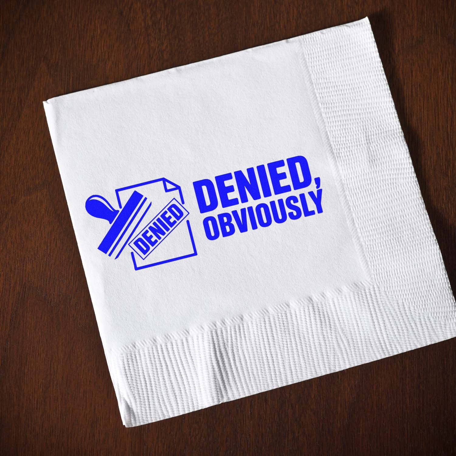 White napkin on wood with bold blue denied stamp and seal reading DENIED, OBVIOUSLY