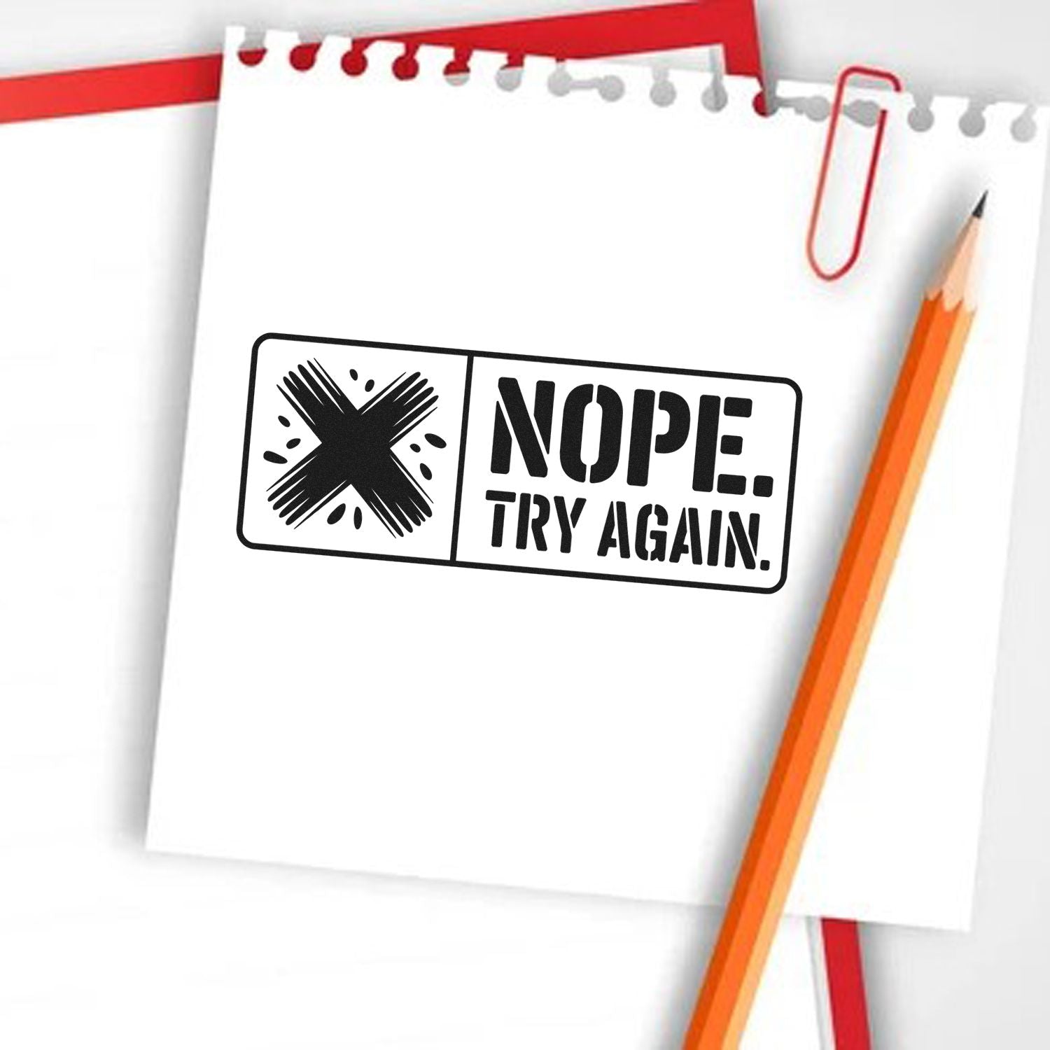 Black rubber stamp reading NOPE. TRY AGAIN. on white paper, with an orange pencil and red paperclip.