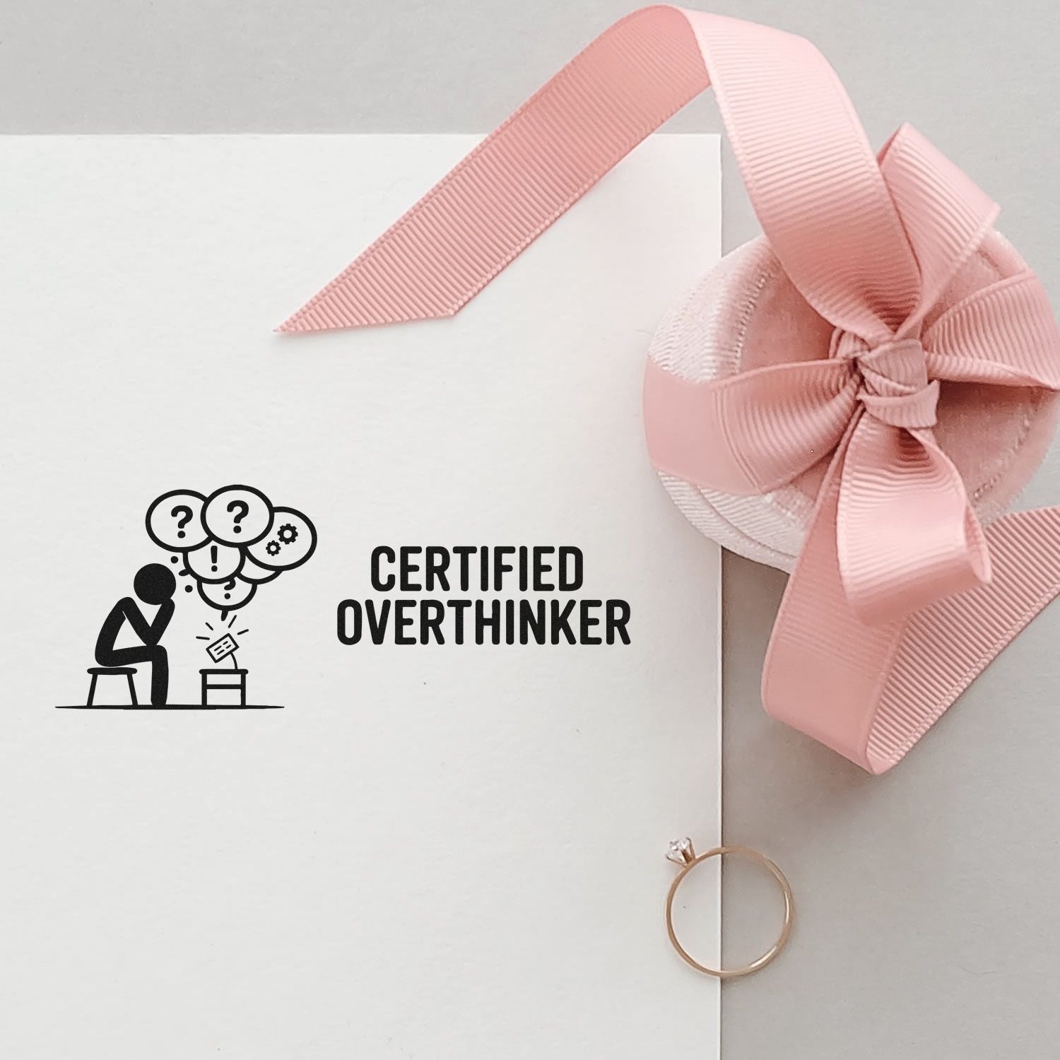 White envelope stamp reading CERTIFIED OVERTHINKER with black icon, pink ribbon bow seal, and gold ring accent.