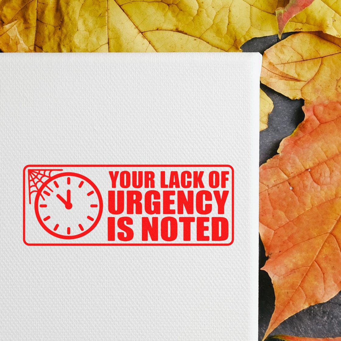Red rubber stamp seal reading Your Lack of Urgency Is Noted with clock icon on white paper, set on autumn leaves.