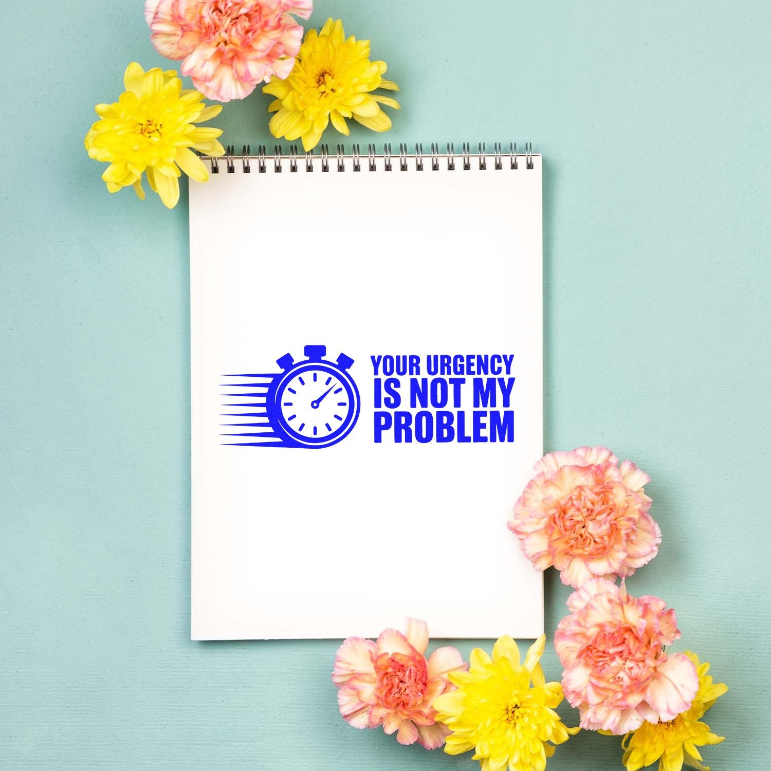Blue self-inking stamp seal reading Your urgency is not my problem on a white notebook, with pink and yellow flowers.