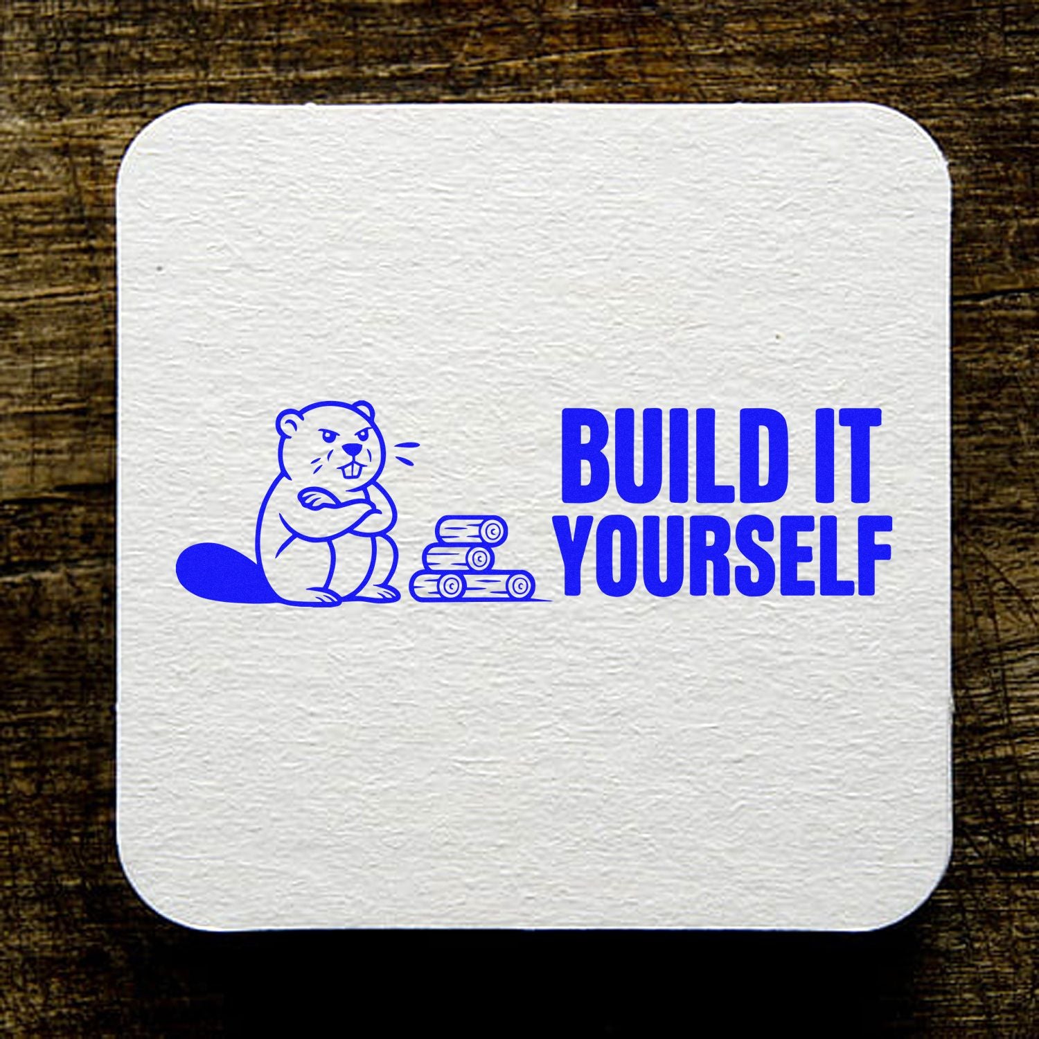 Blue custom stamp seal with beaver and logs, BUILD IT YOURSELF text on a white textured square over a wood background.