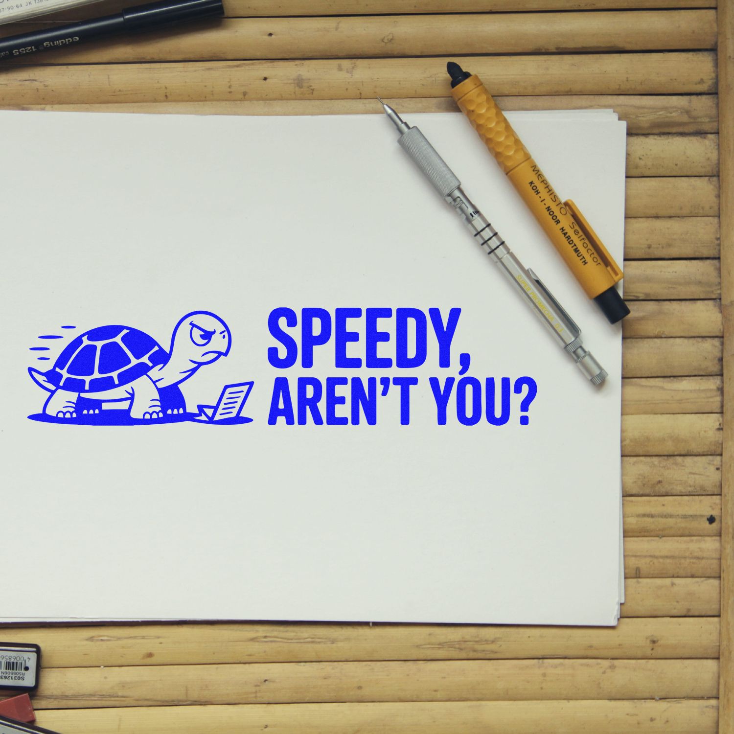 Blue stamp seal with turtle and Speedy, arent you? on white paper, beside pens on a wooden desk.