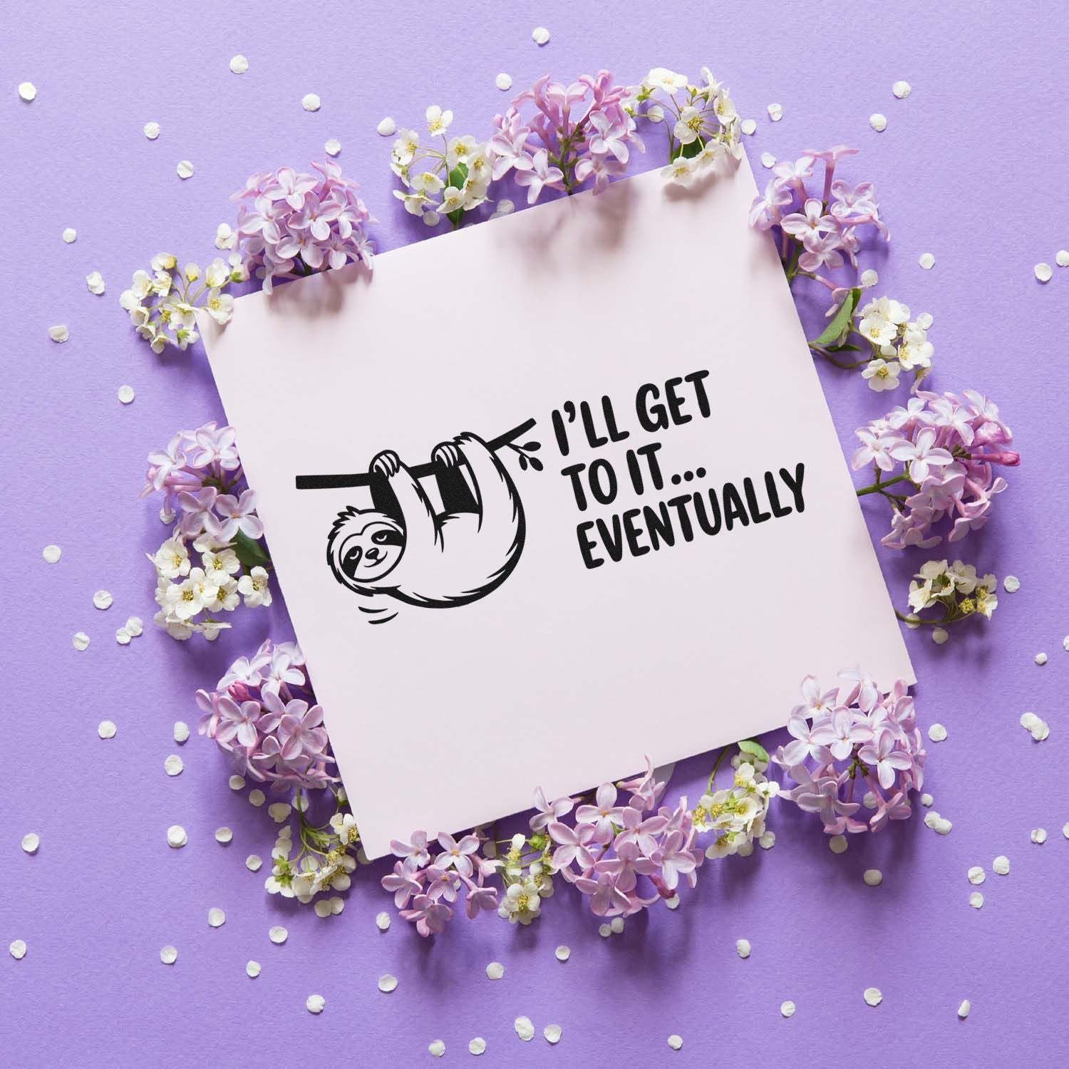 Black sloth stamp design with Ill get to it eventually on pale pink paper, surrounded by lilac and white flowers.