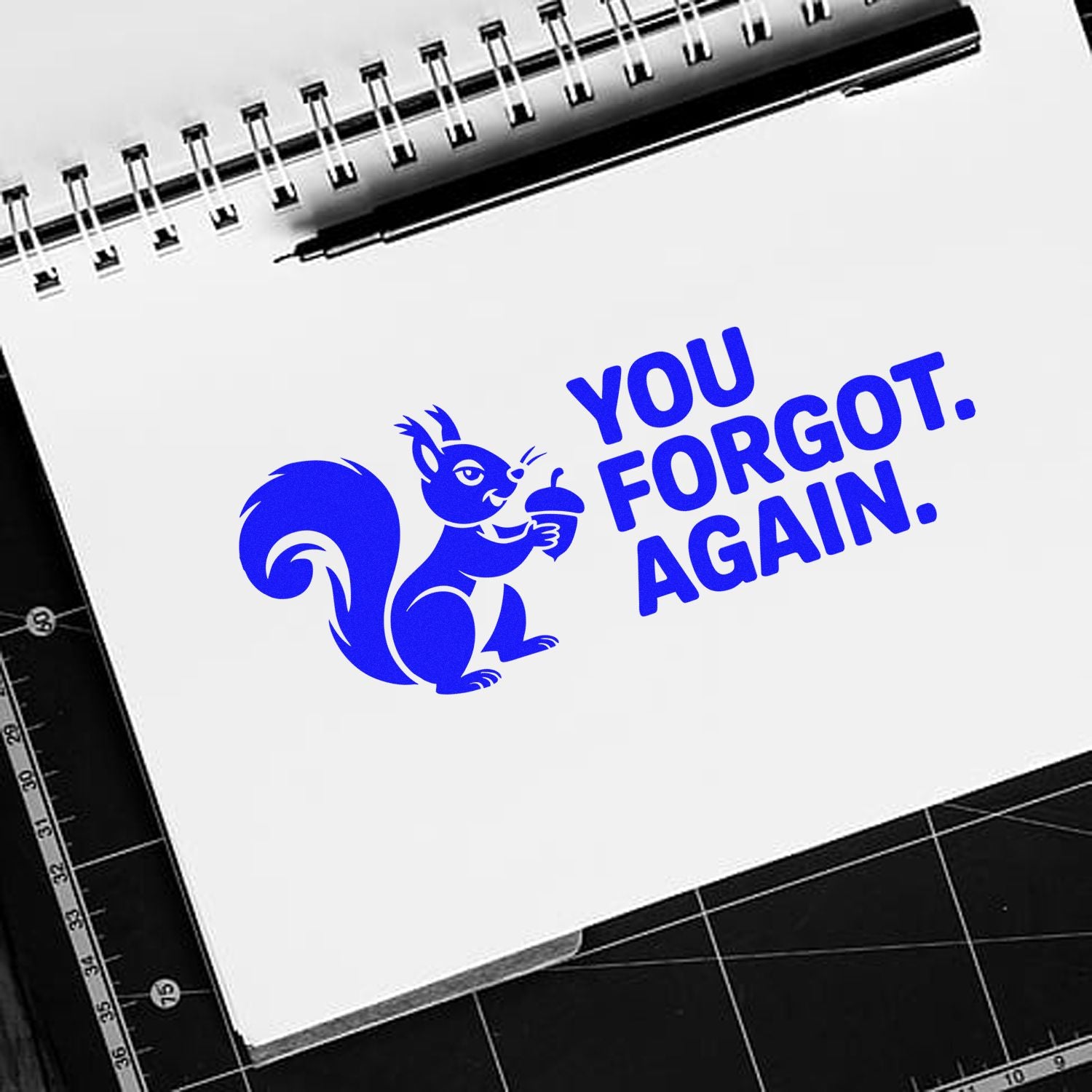 Blue stamp/seal design with squirrel and YOU FORGOT AGAIN on a white notebook page with black spiral binding.