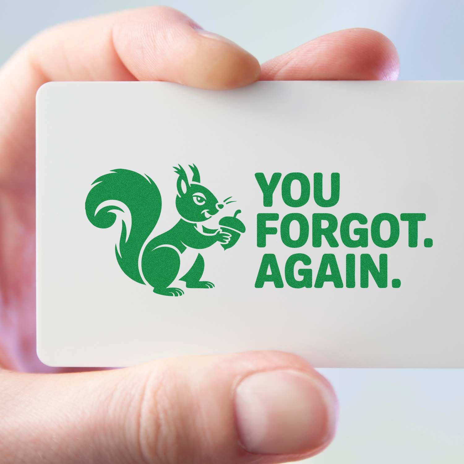 Handheld white stamp and seal card with green squirrel logo and bold green YOU FORGOT. AGAIN. text.